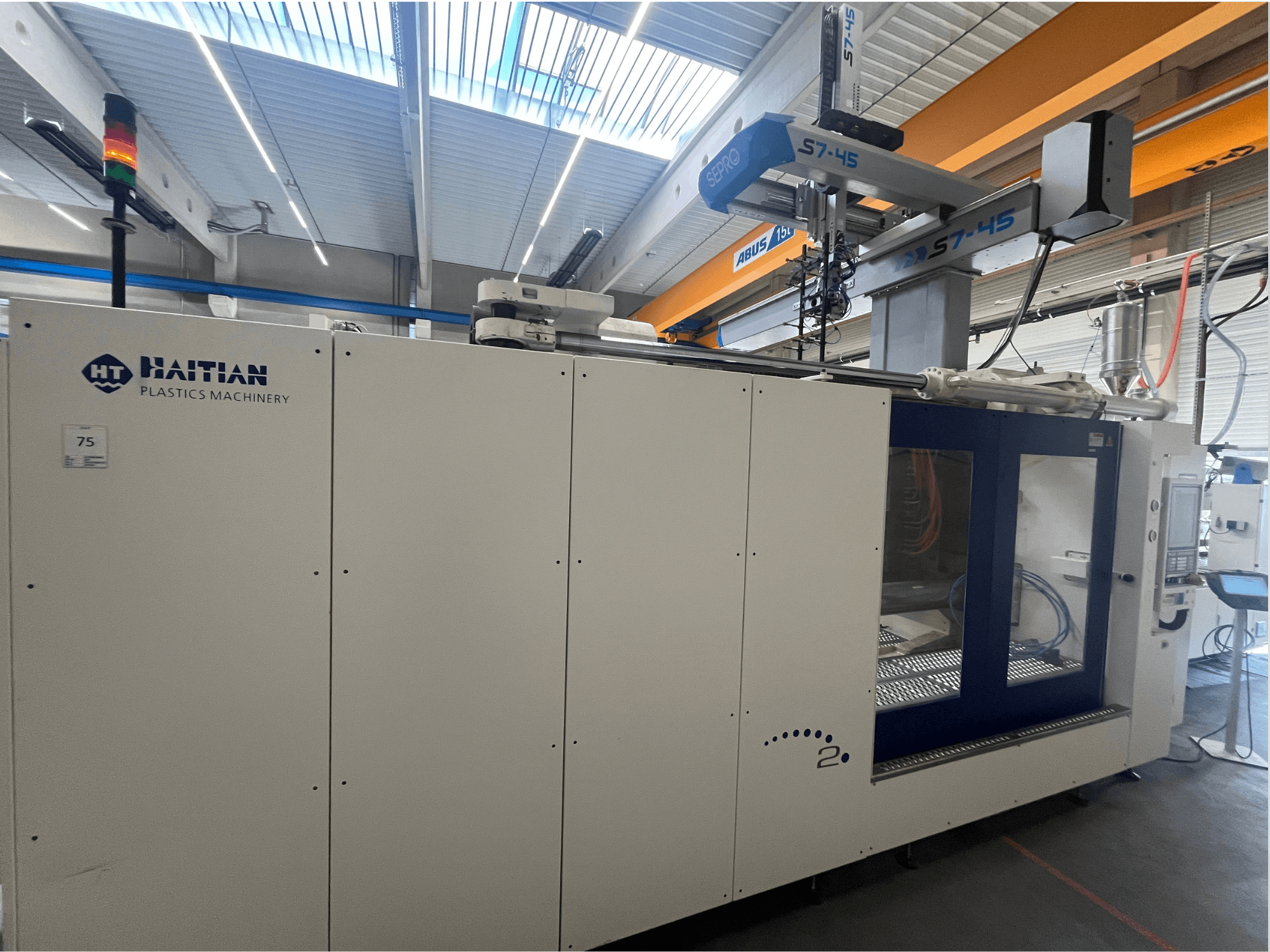 Macchina ad iniezione Haitian S7-45 in vista laterale con pannello di controllo e indicatore luminoso di sicurezza. Design bianco e blu.