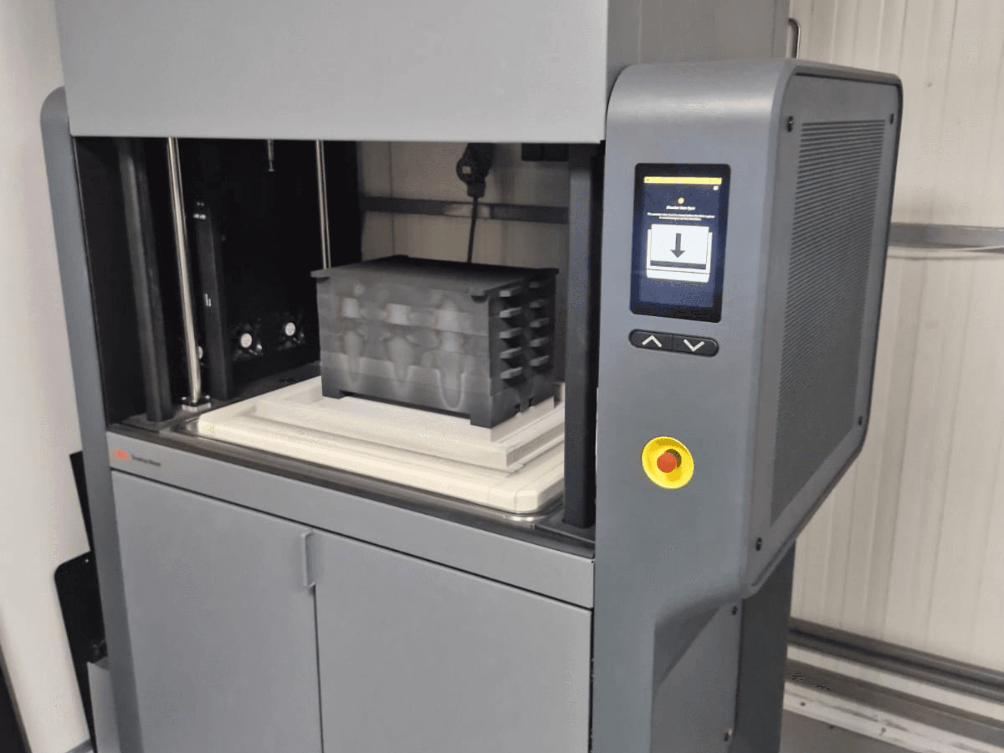 Stampante 3D Metal Studio 2 di Desktop Metal, vista frontale che mostra il pannello di controllo e il letto di stampa con un contenitore nero.