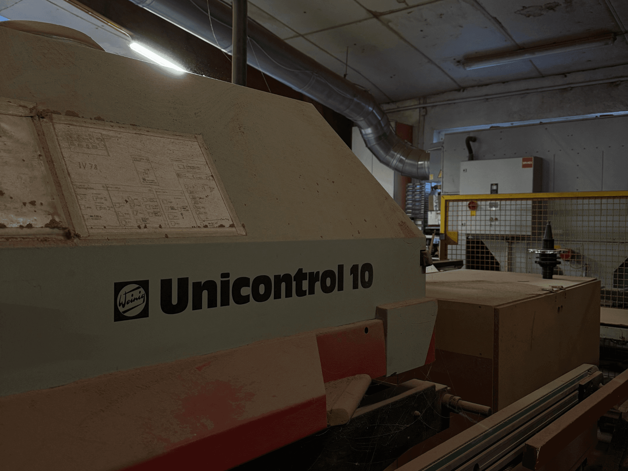 Macchina Weinig Unicontrol 10 vista da un'angolazione laterale, superficie polverosa, schemi tecnici visibili sul pannello frontale.