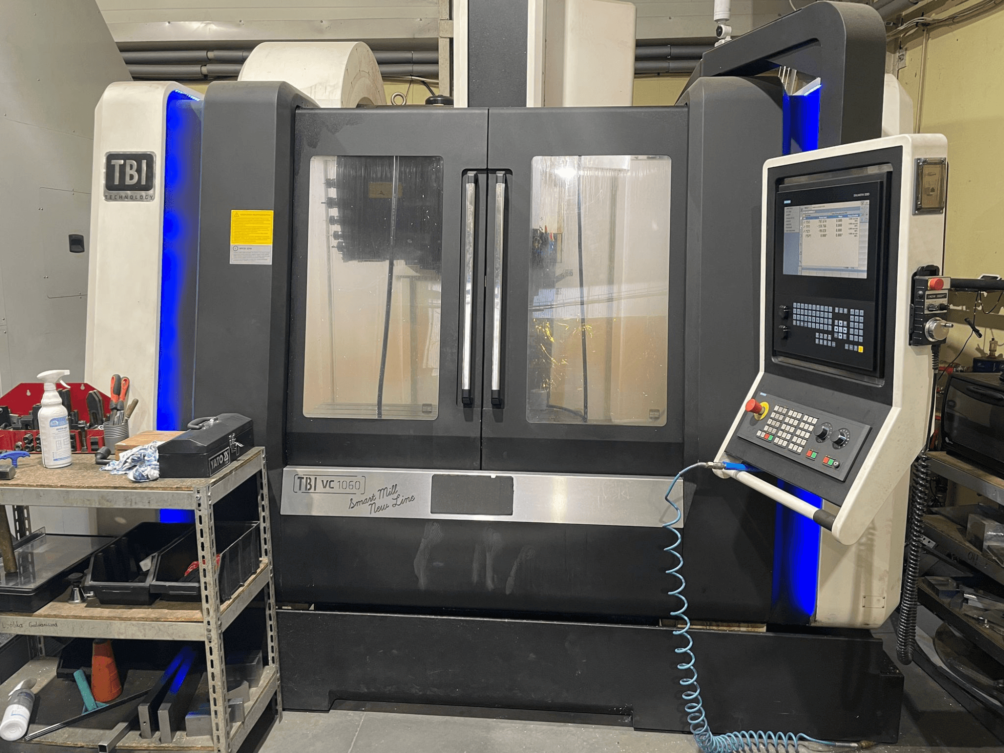 Centro di lavoro verticale TBI VC 1060 HH, vista frontale, con pannello di controllo, coperchio antipolvere e accenti blu illuminati.
