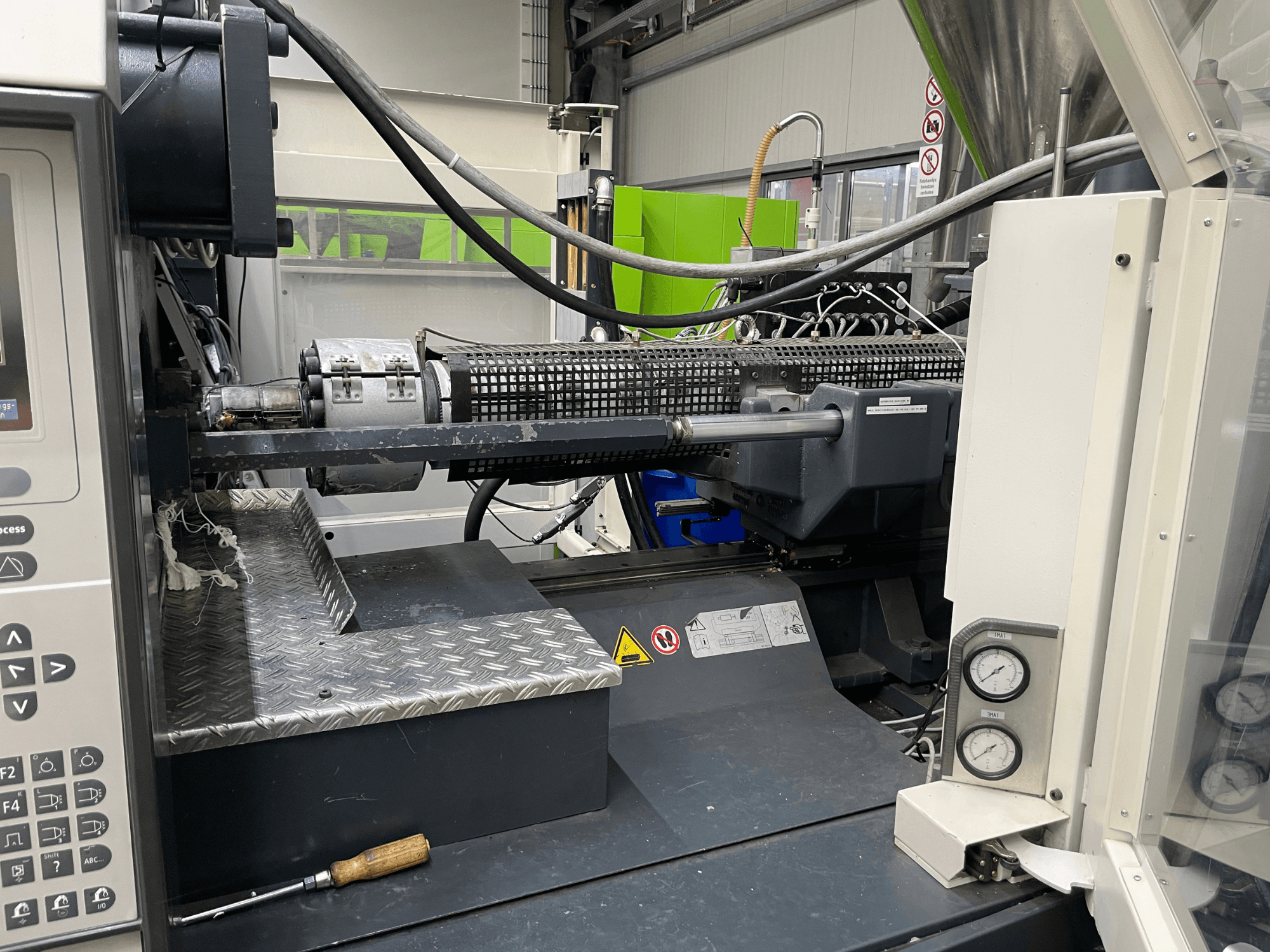 Vista laterale della macchina di stampaggio a iniezione con pannello di controllo, estrusore e manometri visibili, ideale per le attività di produzione.