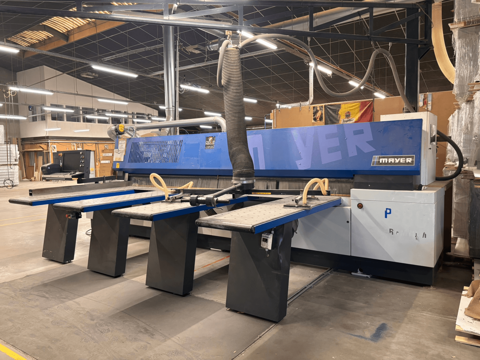 Macchina CNC Mayer con pannelli blu, vista frontale; dispone di più tavoli di lavoro e di un sistema di aspirazione delle polveri per la lavorazione del legno.