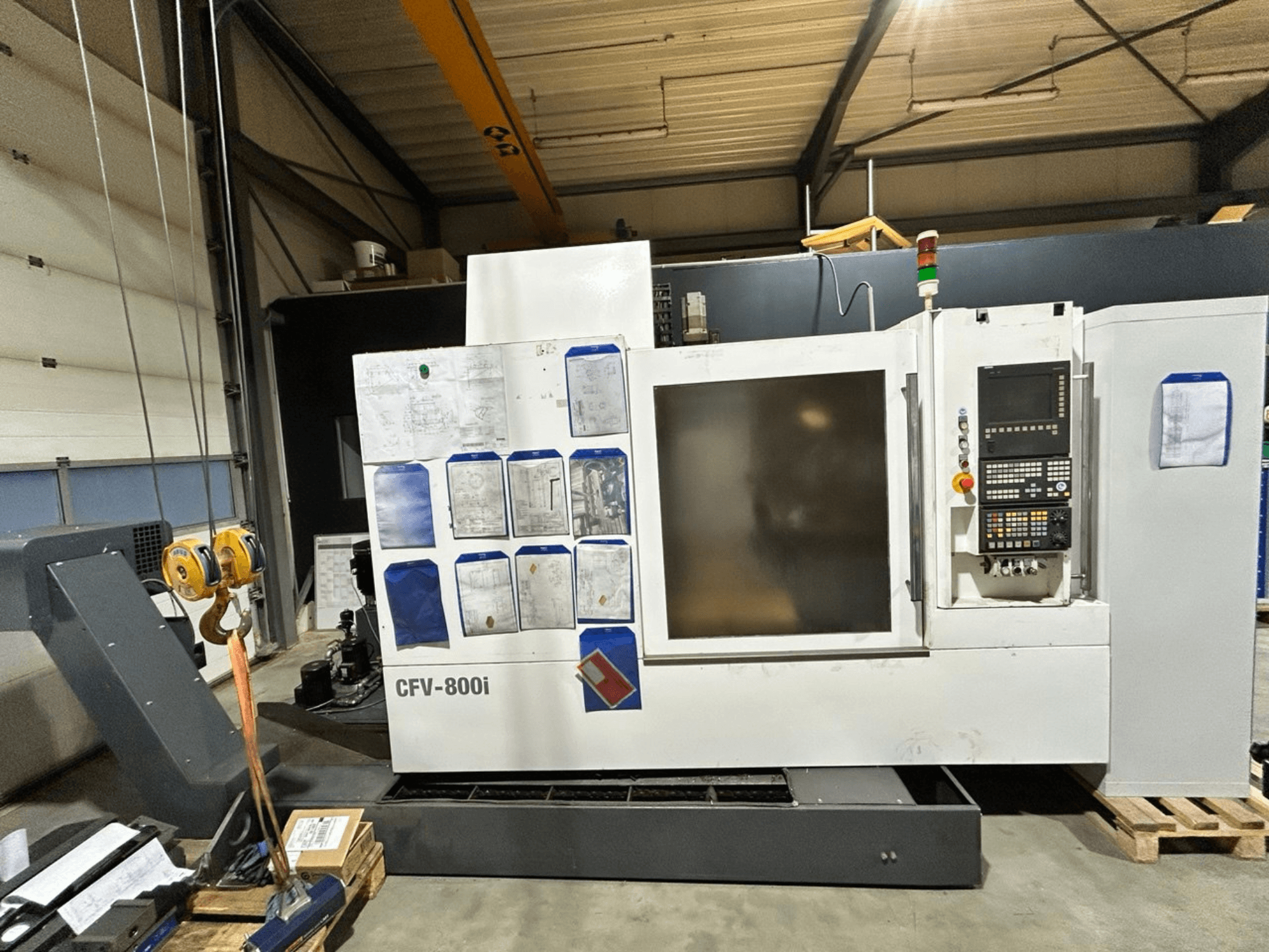 Macchina CNC CFV-800i in vista frontale, con pannello di controllo, documenti a lato e carroponte in un'ambientazione di fabbrica.