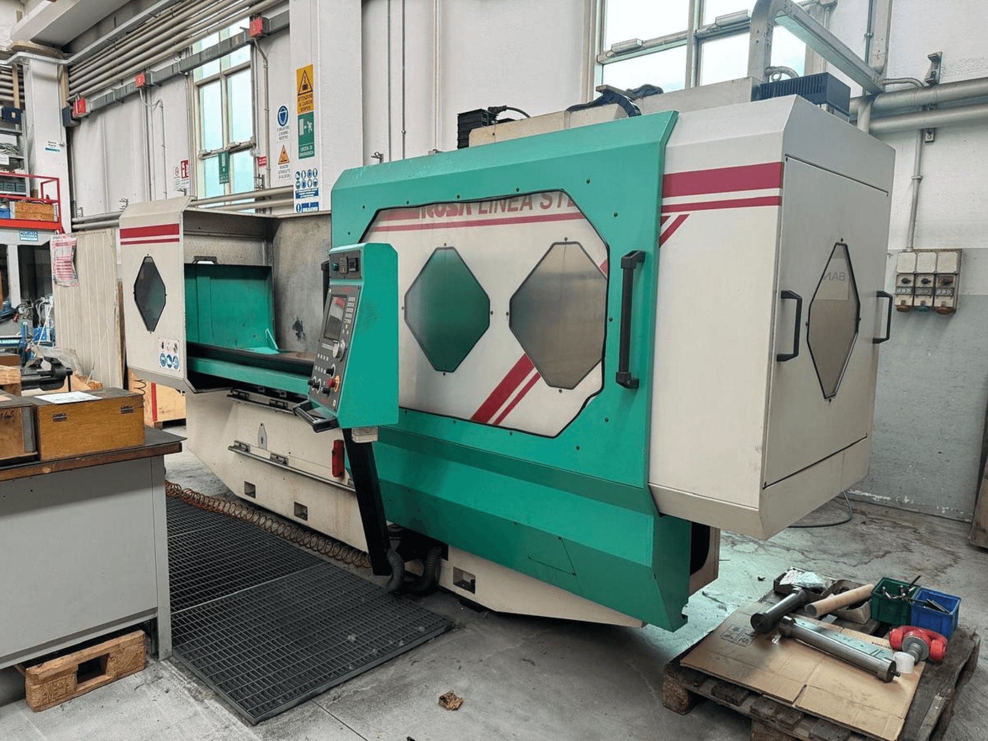 Macchina di precisione verde e bianca, vista frontale, con pannello di controllo, area di lavoro e utensili su un pallet. Marchio: BAMB.