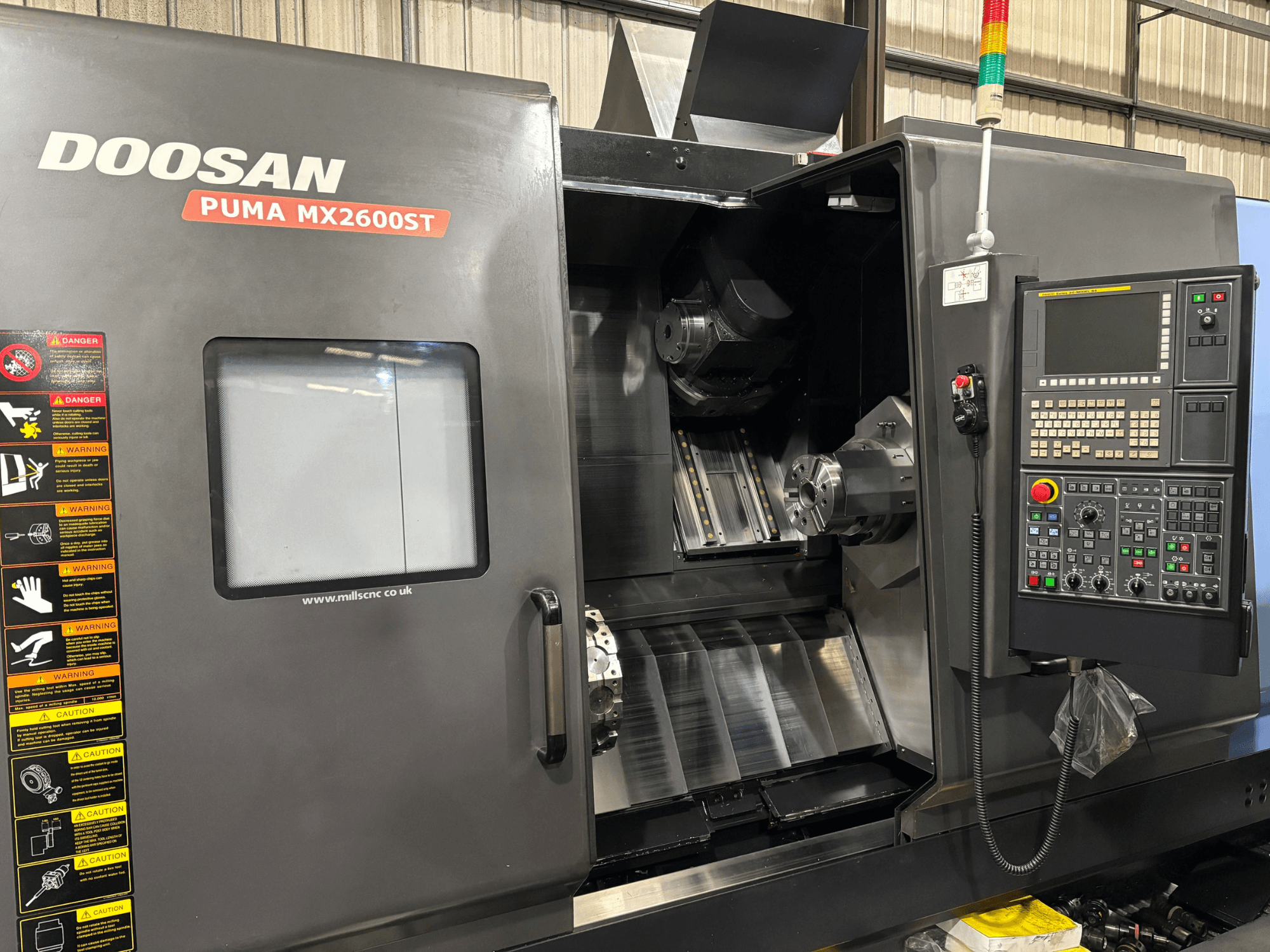 Tornio CNC Doosan PUMA MX2600ST, vista frontale, con pannello di controllo, mandrino e area di lavorazione con avvisi di sicurezza visibili.