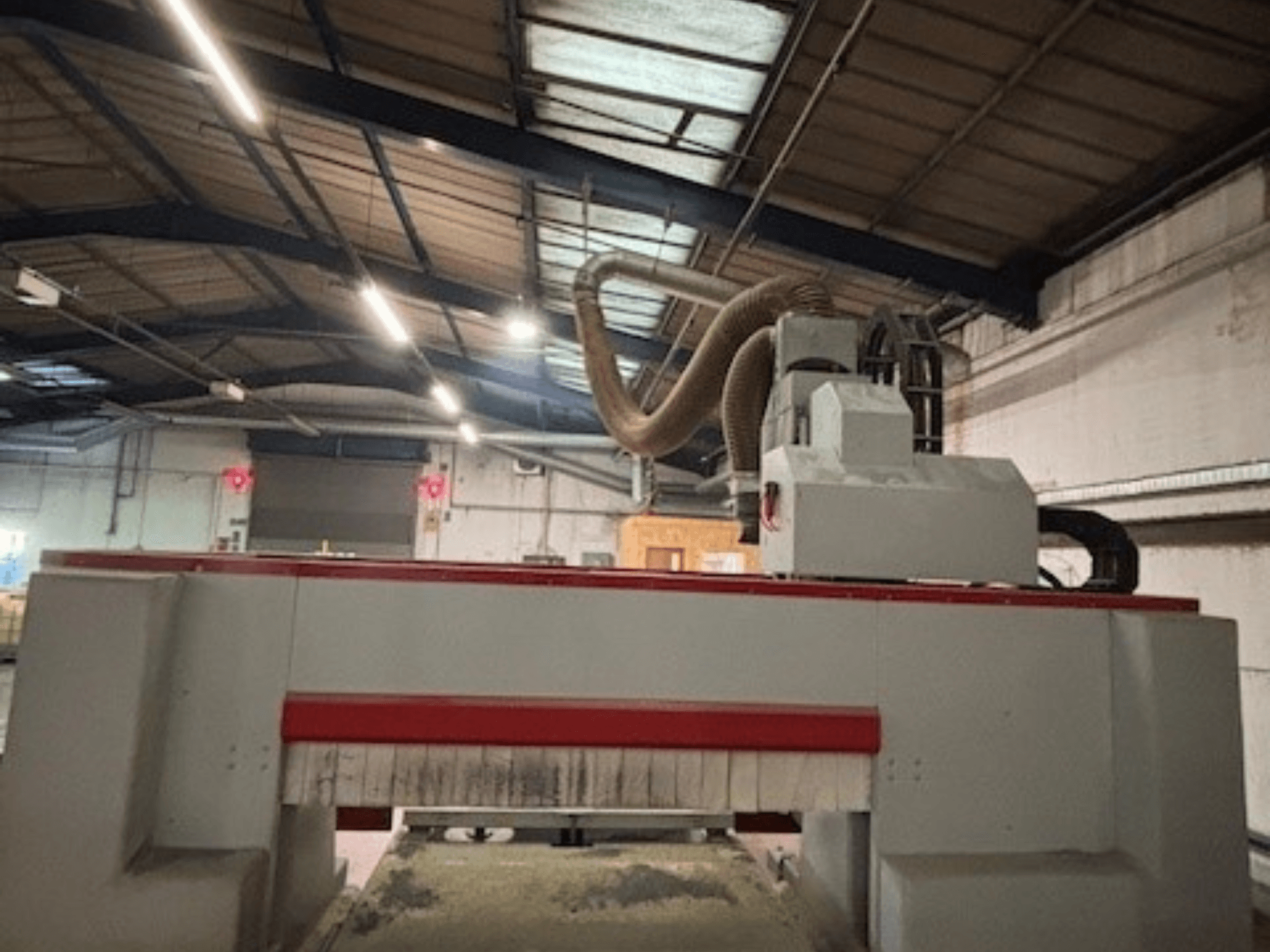 Macchina per fresatura CNC in un'officina, vista laterale che evidenzia il design rosso e grigio, sistema di aspirazione della polvere collegato.