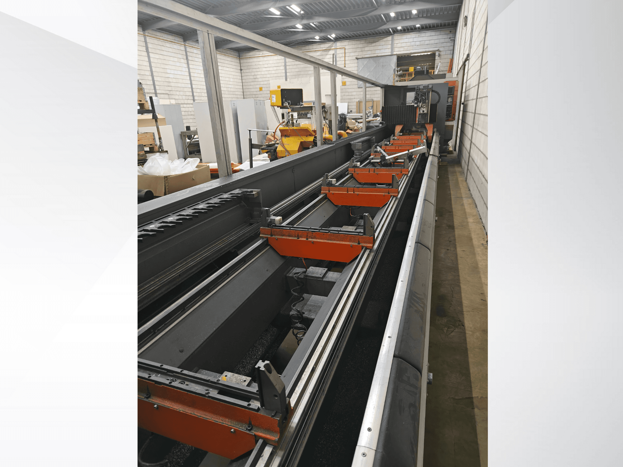 Vista laterale di una macchina CNC industriale, con guide lineari, morsetti arancioni e componenti di precisione in un magazzino.