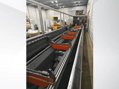 Vista laterale di una macchina CNC industriale, con guide lineari, morsetti arancioni e componenti di precisione in un magazzino.