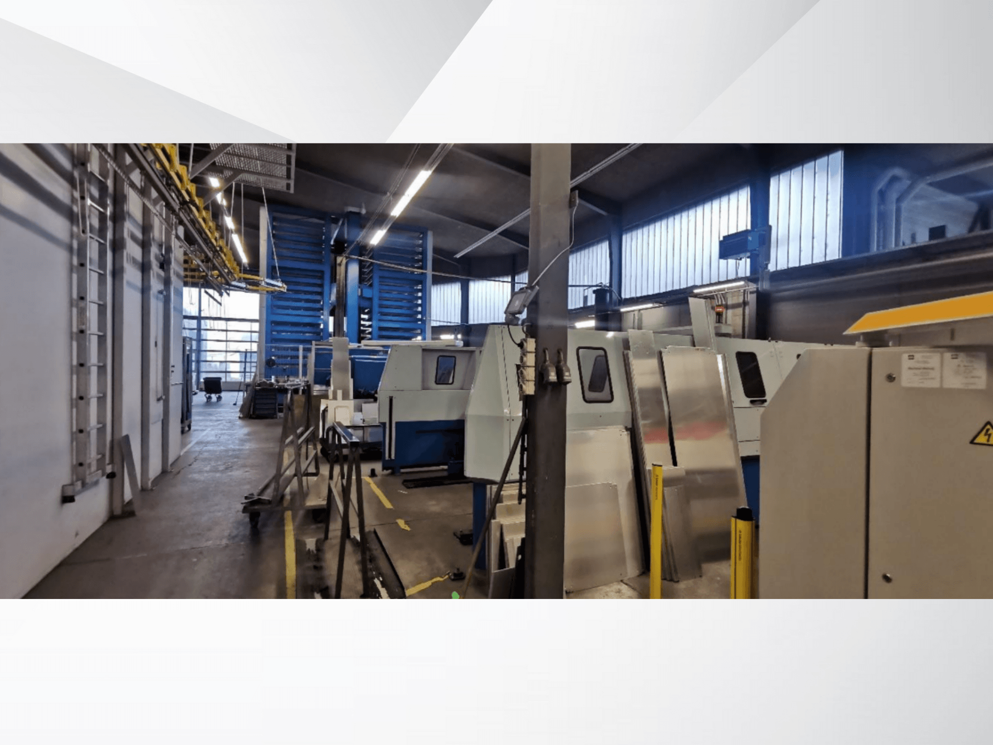Scena di officina industriale con diverse macchine e attrezzature in vista laterale, con superfici metalliche e dispositivi di sicurezza visibili.