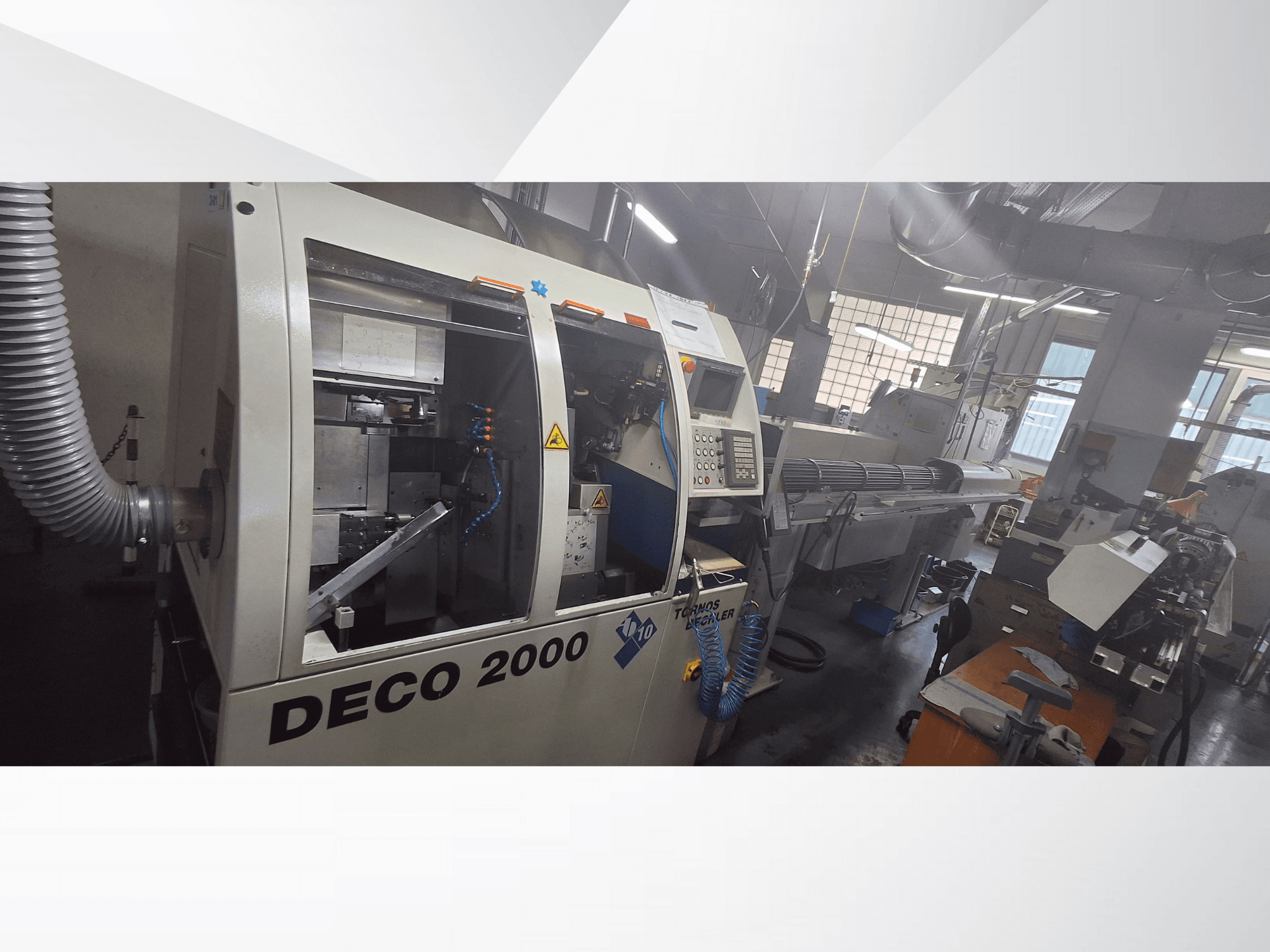 La macchina DECO 2000 CNC in officina, vista frontale, con i comandi e la configurazione di un pezzo lungo sulla destra.