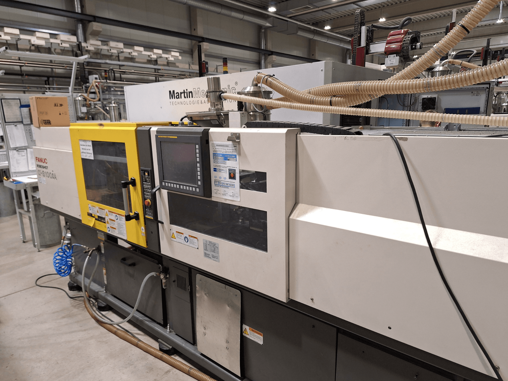 Macchina ad iniezione elettrica FANUC Roboshot S100iA, vista laterale, dotata di touchscreen ed etichette di sicurezza.