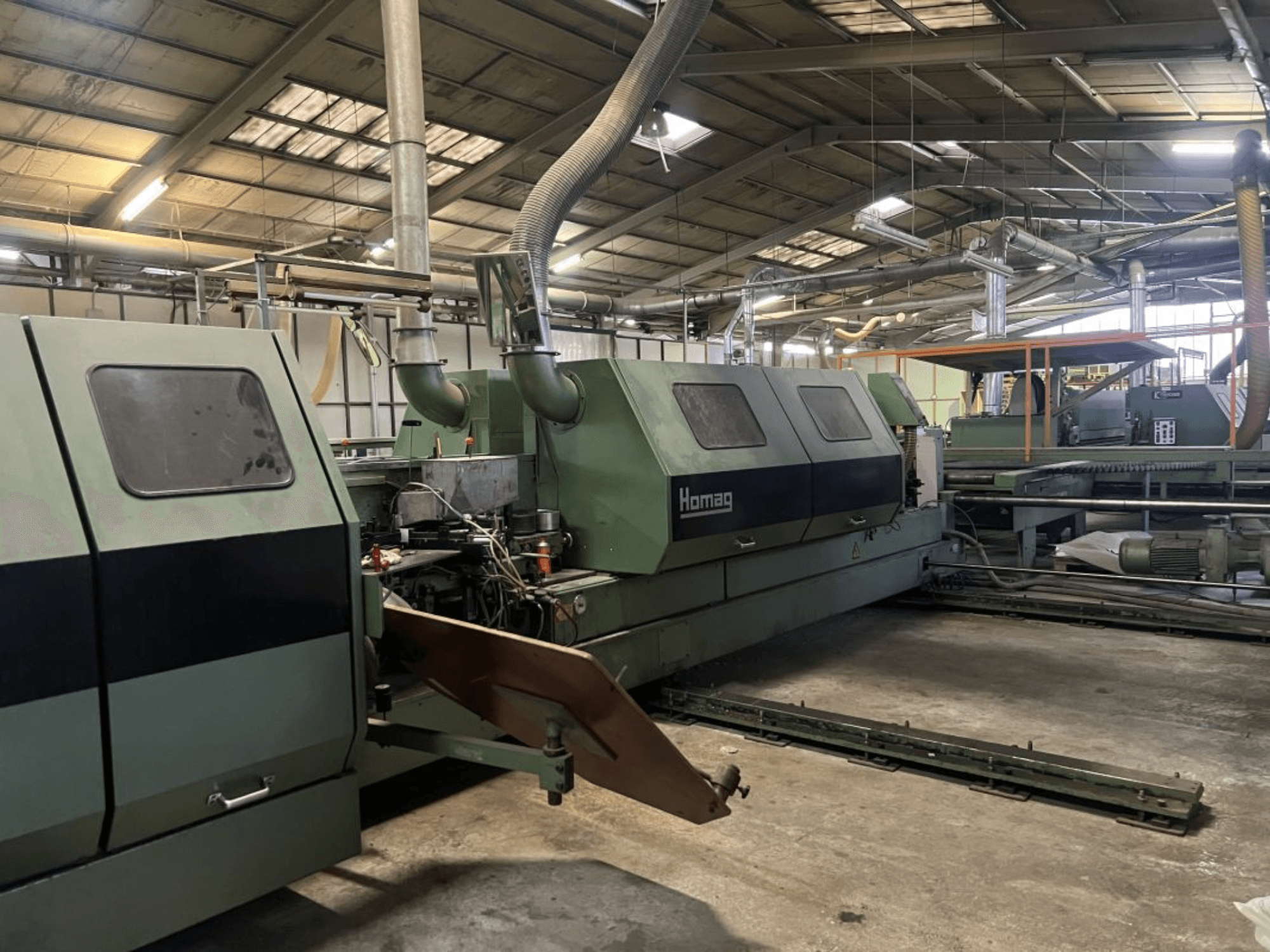 Macchina industriale Homag in verde, vista laterale, con componenti operativi e pannello di controllo visibili in un magazzino.