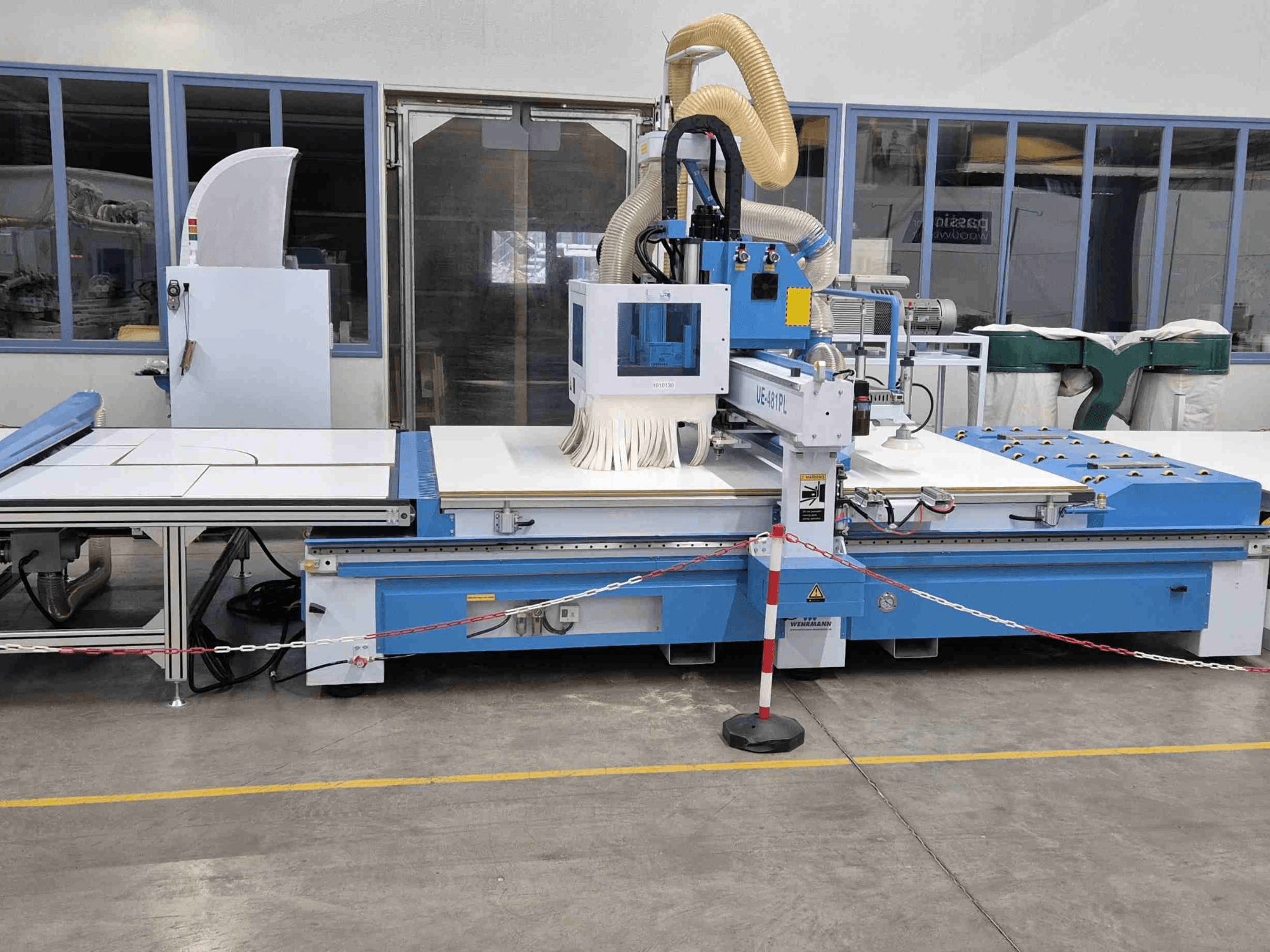 Router CNC blu UE-621PL visto di fronte, con un grande tavolo da taglio e un sistema di aspirazione della polvere collegato.