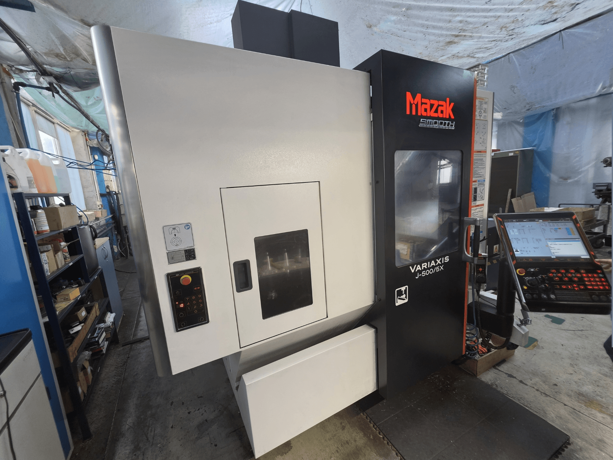 Centro di lavorazione verticale Mazak VARIAXIS J-500/5X visto frontalmente, dotato di pannello di controllo e ampia finestra di visualizzazione dell'area di lavorazione.