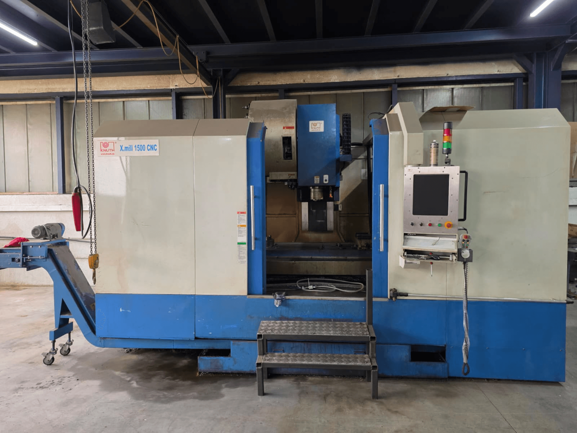Centro di lavorazione verticale CNC KNUTH X-MILL 1500, vista laterale, con pannello di controllo, gradini e nastro trasportatore di uscita.