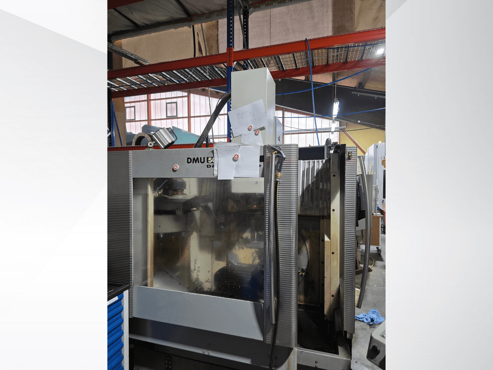 Centro di lavoro CNC a 3 assi DMU 50 in un'officina, visto frontalmente, con componenti operativi e documenti allegati.