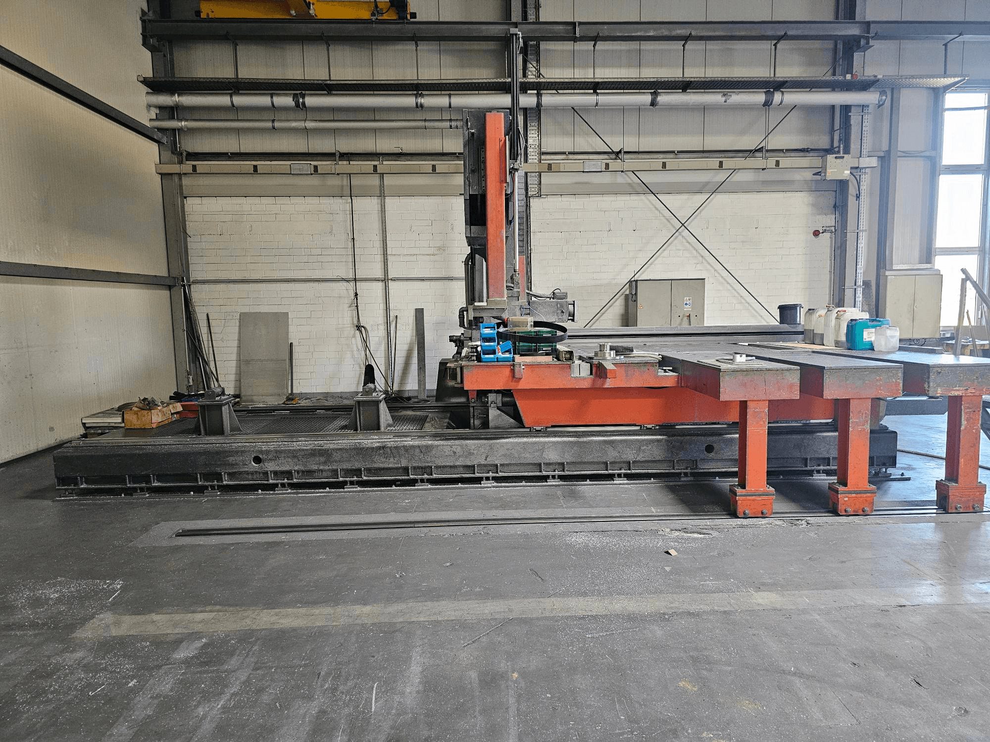 Macchina da taglio industriale in un'officina aperta, arancione e nera con un grande tavolo; vista laterale che mostra gli accessori e lo spazio di lavoro.