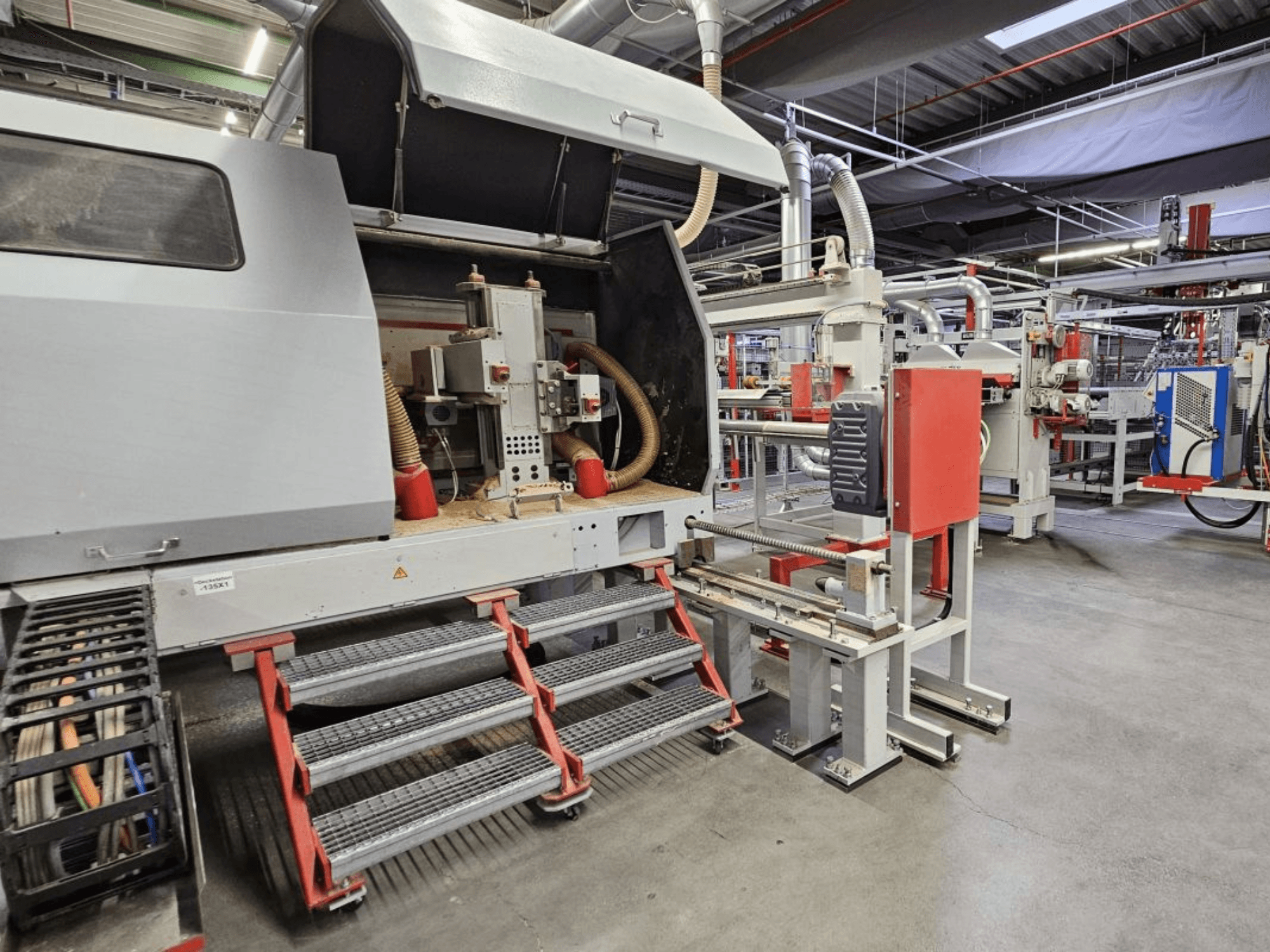 Vista frontale della linea di produzione di legno BURKLE Optima 1428/50, con gradini e componenti visibili del macchinario.