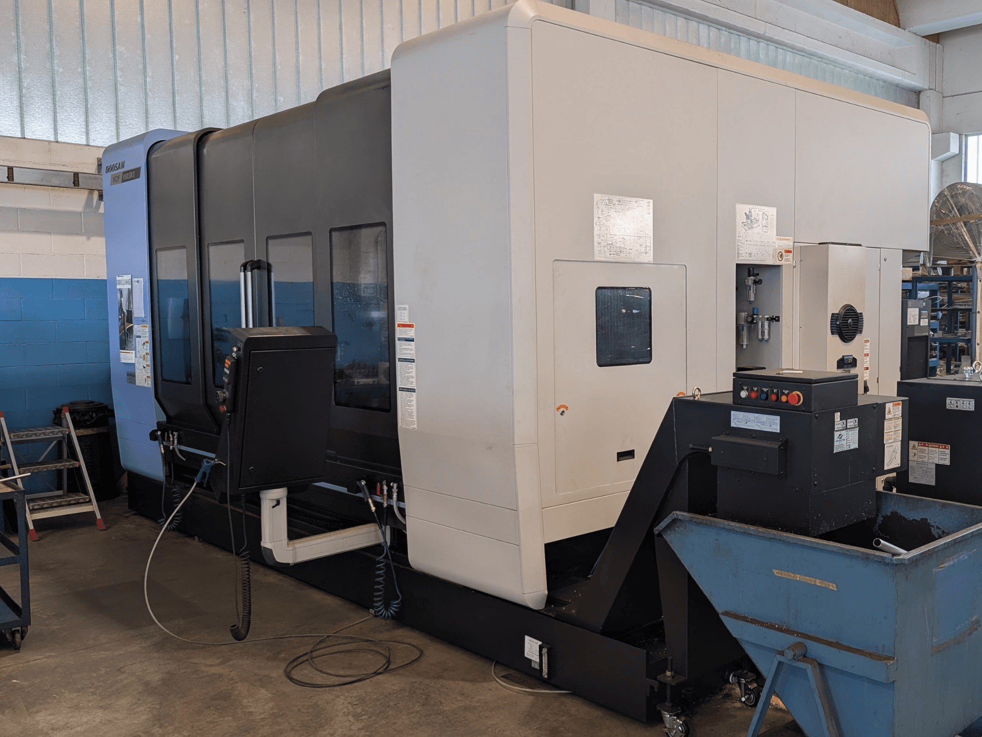 Centro di lavorazione verticale DOOSAN VCF850LSR-II visto di profilo, con in primo piano il pannello di controllo, il sistema di raffreddamento e la struttura robusta.