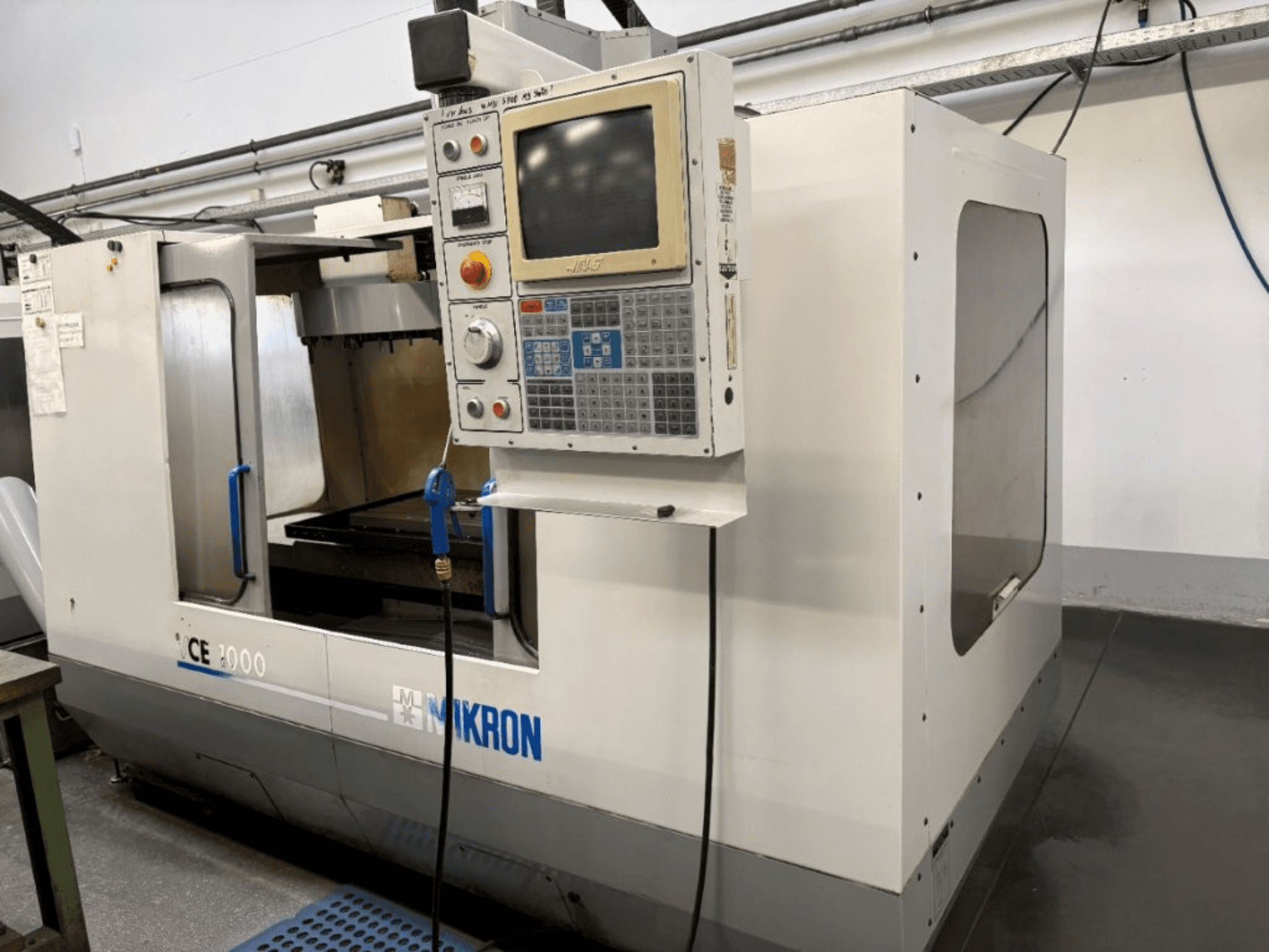 Macchina CNC Mikron CE 2000, vista frontale; presenta un pannello di controllo con pulsanti e schermo, esterno argentato e area di lavoro.