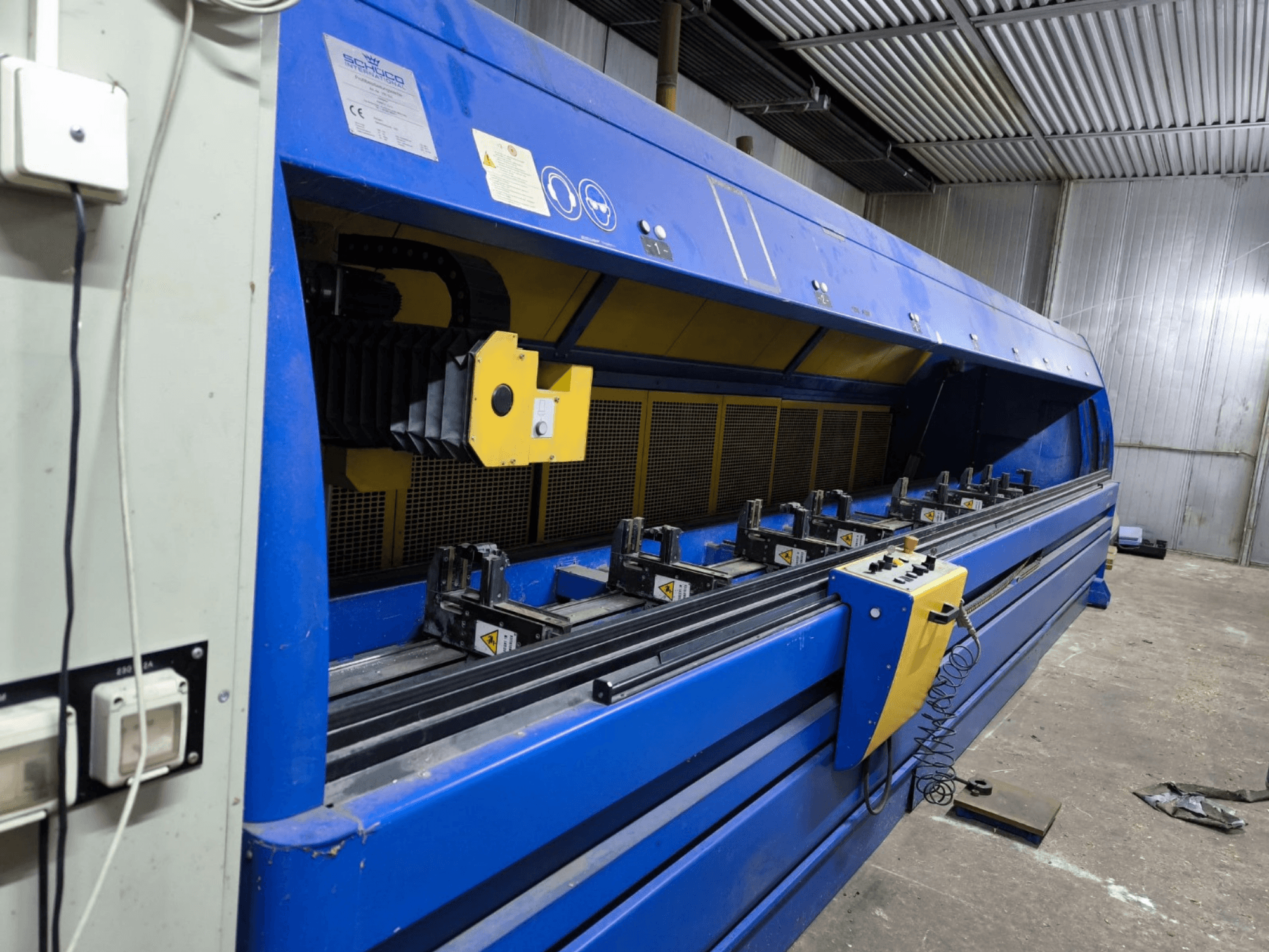 Macchina da taglio industriale Schneider in blu, vista laterale, con pannello di controllo, nastri e stazioni di serraggio multiple visibili.