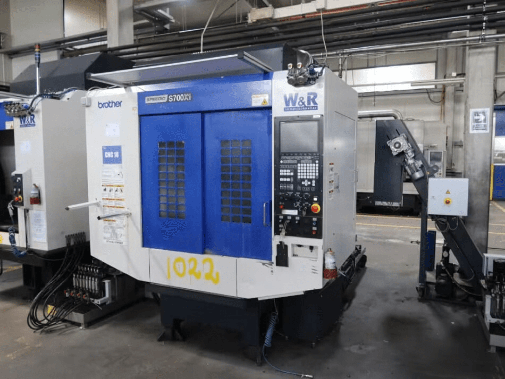 Centro di lavorazione verticale Brother Speedio S700 X1, vista frontale, con pannello di controllo e sportelli blu, in un ambiente industriale.