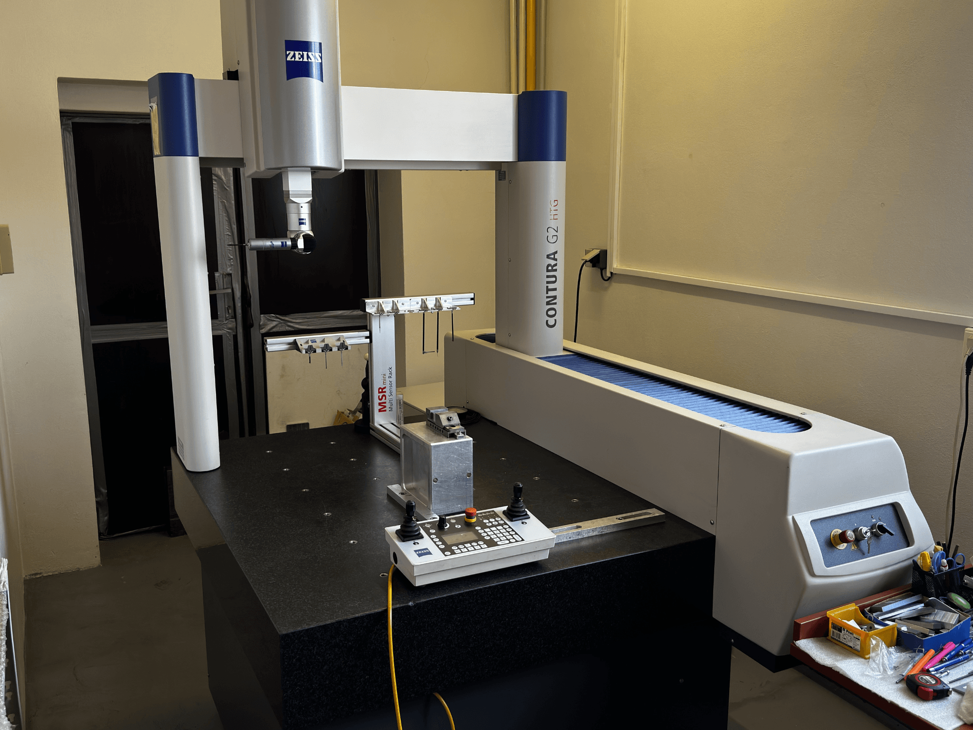 CMM ZEISS Contura G2 in un laboratorio, vista frontale che mostra il braccio di misura, il pannello di controllo e l'area di lavoro adiacente.