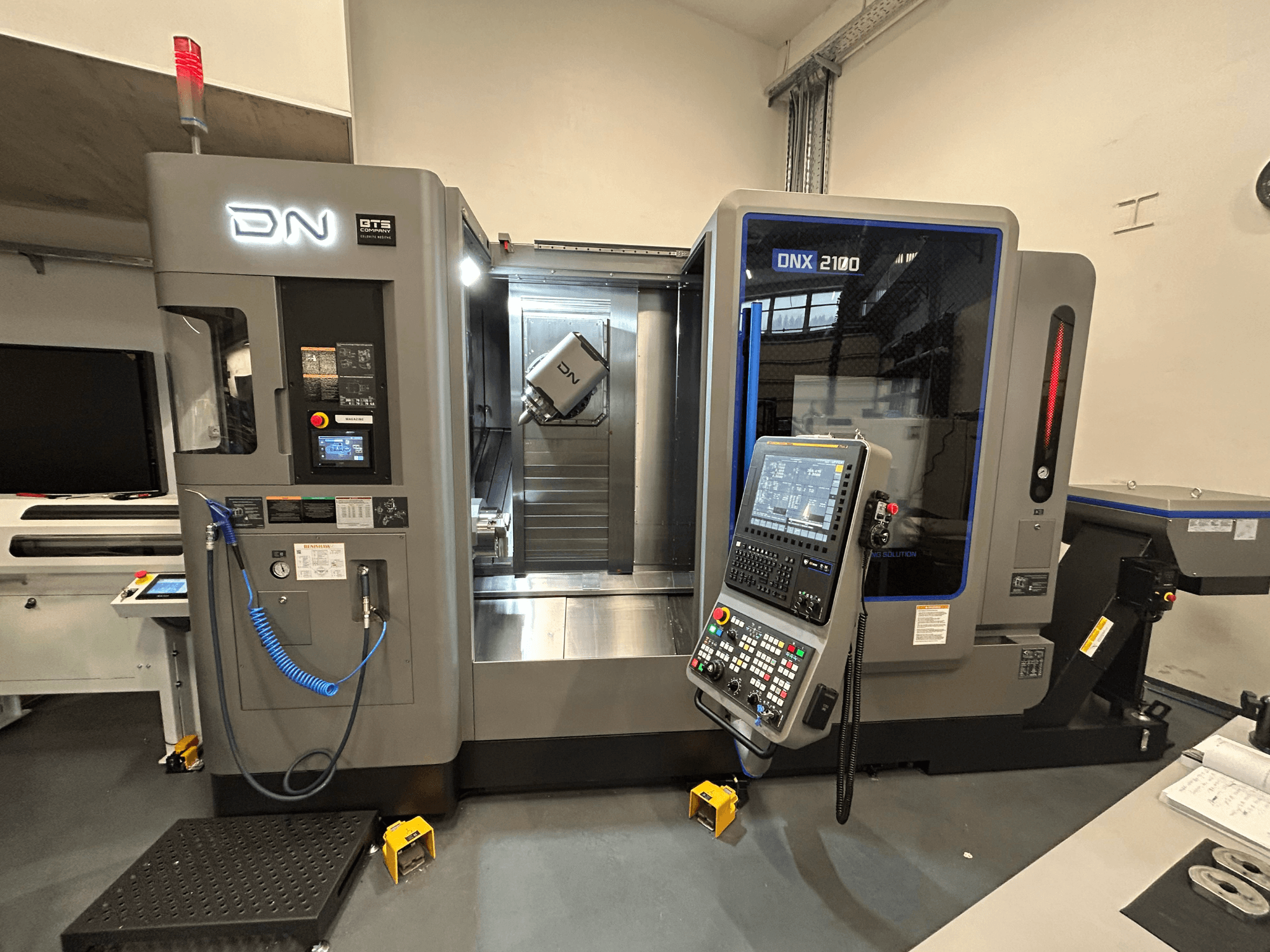Macchina CNC DN ONX 2100, vista frontale, con pannello di controllo, area di lavoro e utensile. Dotata di luce di sicurezza e indicatori di funzionamento.