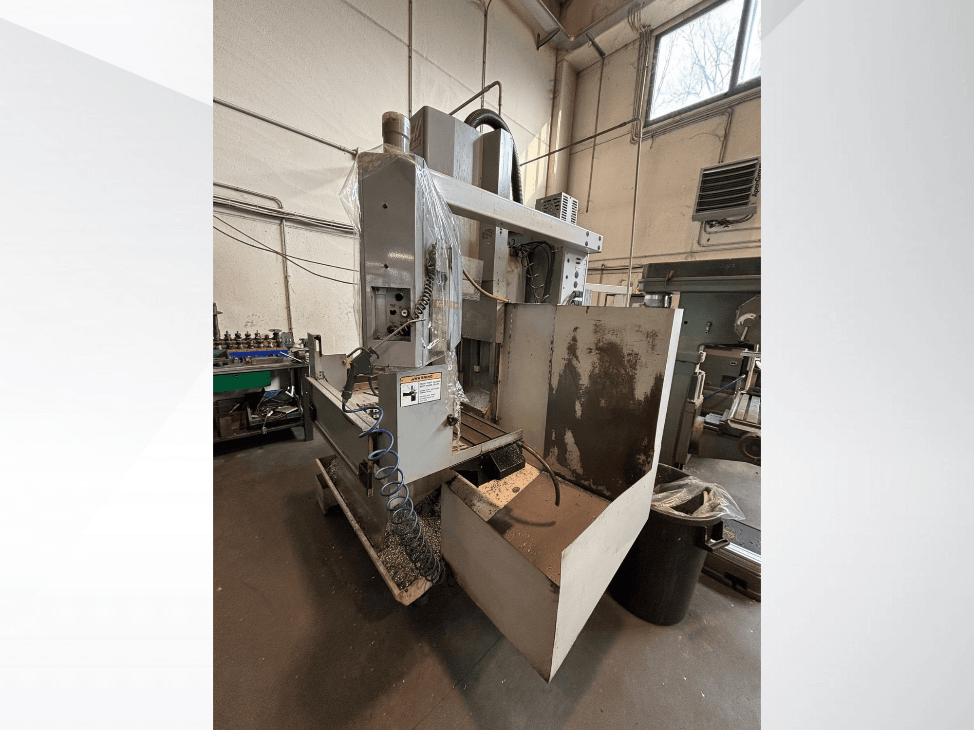 Fresatrice verticale con coperchio di protezione, vista laterale; include il tubo del refrigerante e il pannello di controllo visibile. Ideale per la lavorazione.