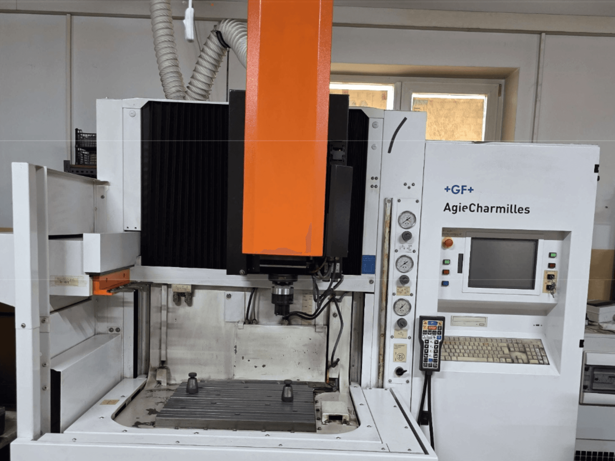 Centro di lavoro AgieCharmilles in vista frontale con un grande mandrino arancione, pannello di controllo e tavolo di lavoro visibile.