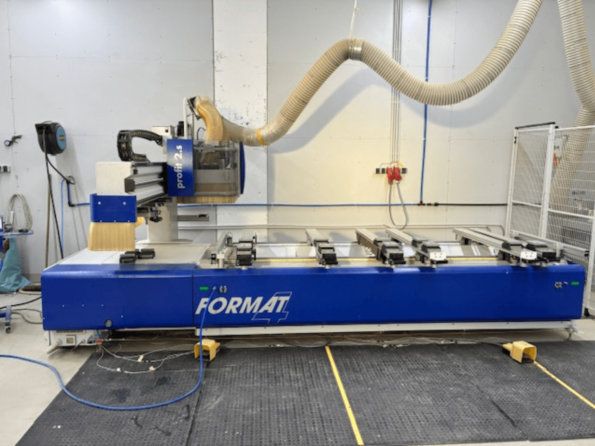 Router CNC FORMAT 4 blu, modello Profit 2.5, vista laterale che mostra l'area di taglio e il sistema di aspirazione della polvere, su un tappetino di gomma.