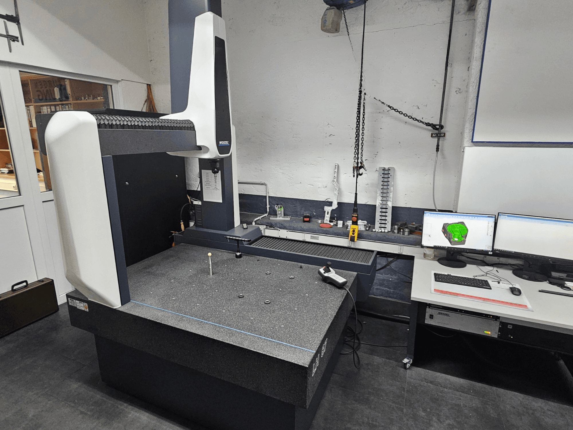 Macchina di misura a coordinate Wenzel LH 87 in un'officina, vista frontale, con una sonda sul tavolo di granito e doppio monitor che visualizza il progetto CAD.