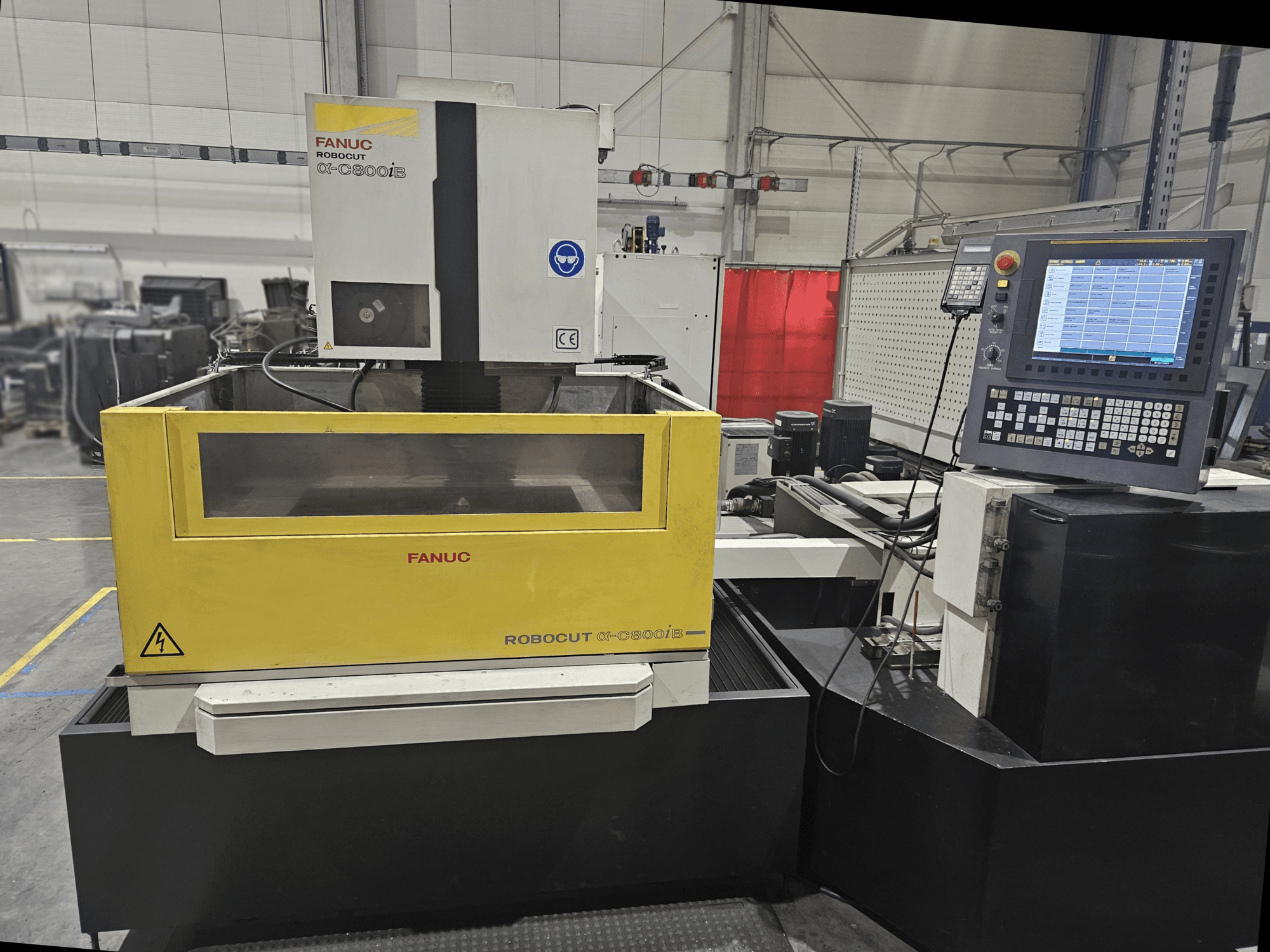 Vista frontale di FANUC Robocut α-C600iB con corpo macchina giallo e grigio, pannello di controllo CNC e display operativo.