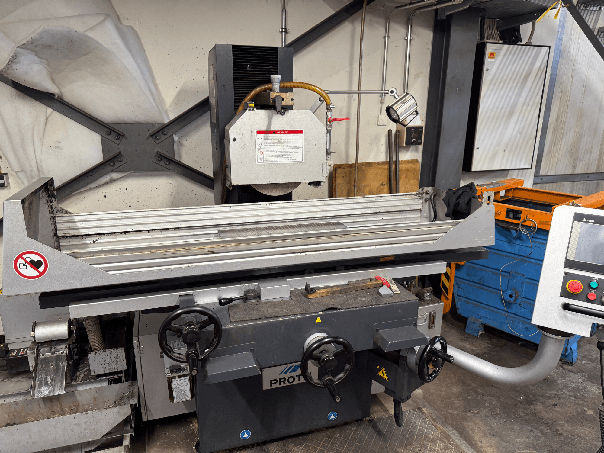 Macchina PROTEC, vista frontale, che mostra una smerigliatrice per superfici con comandi manuali, avvertenze di sicurezza e sistema di raffreddamento.