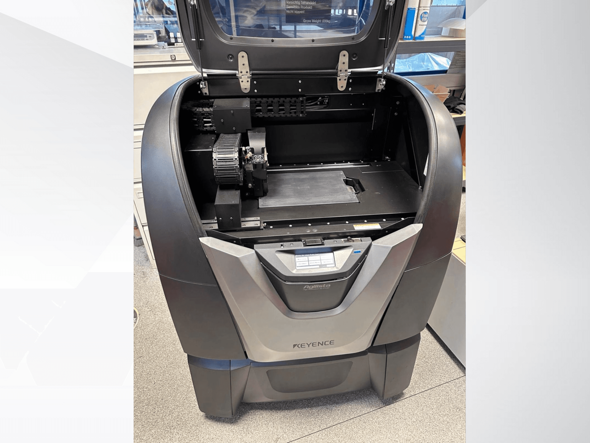 La stampante 3D KEYENCE Agilista, vista frontale, rivela la parte superiore aperta, l'ampia piattaforma di costruzione e i componenti meccanici interni.