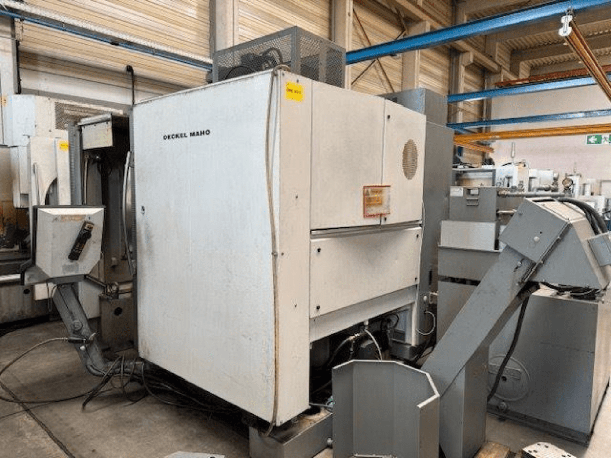 Centro di lavoro verticale DECKEL MAHO DMC 100 V, vista laterale con pannello di controllo e vari accessori visibili.