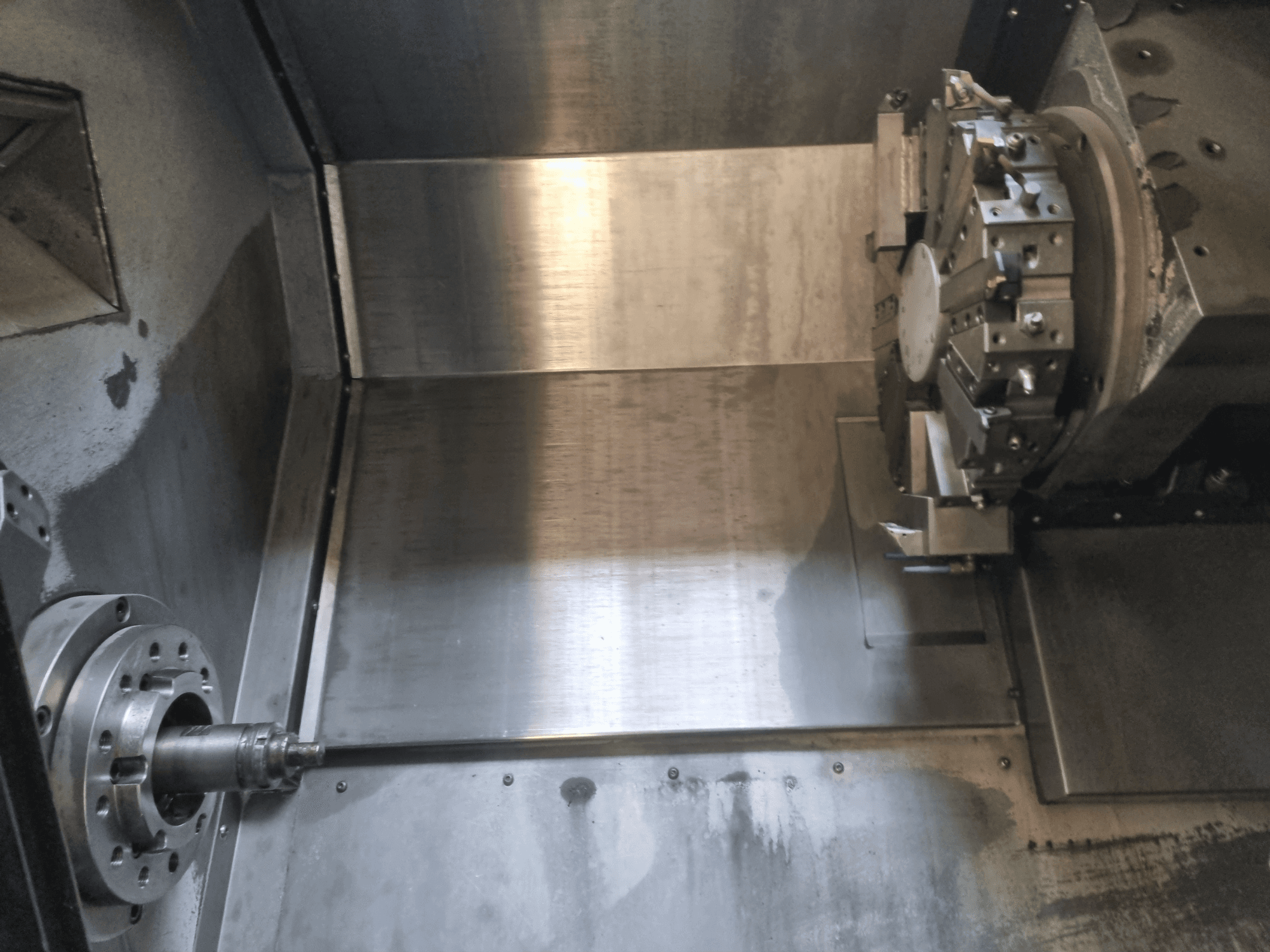 Vista interna di un tornio CNC, caratterizzato da un mandrino rotante e da una superficie di lavoro in metallo, che mostra l'ingegneria industriale di precisione.