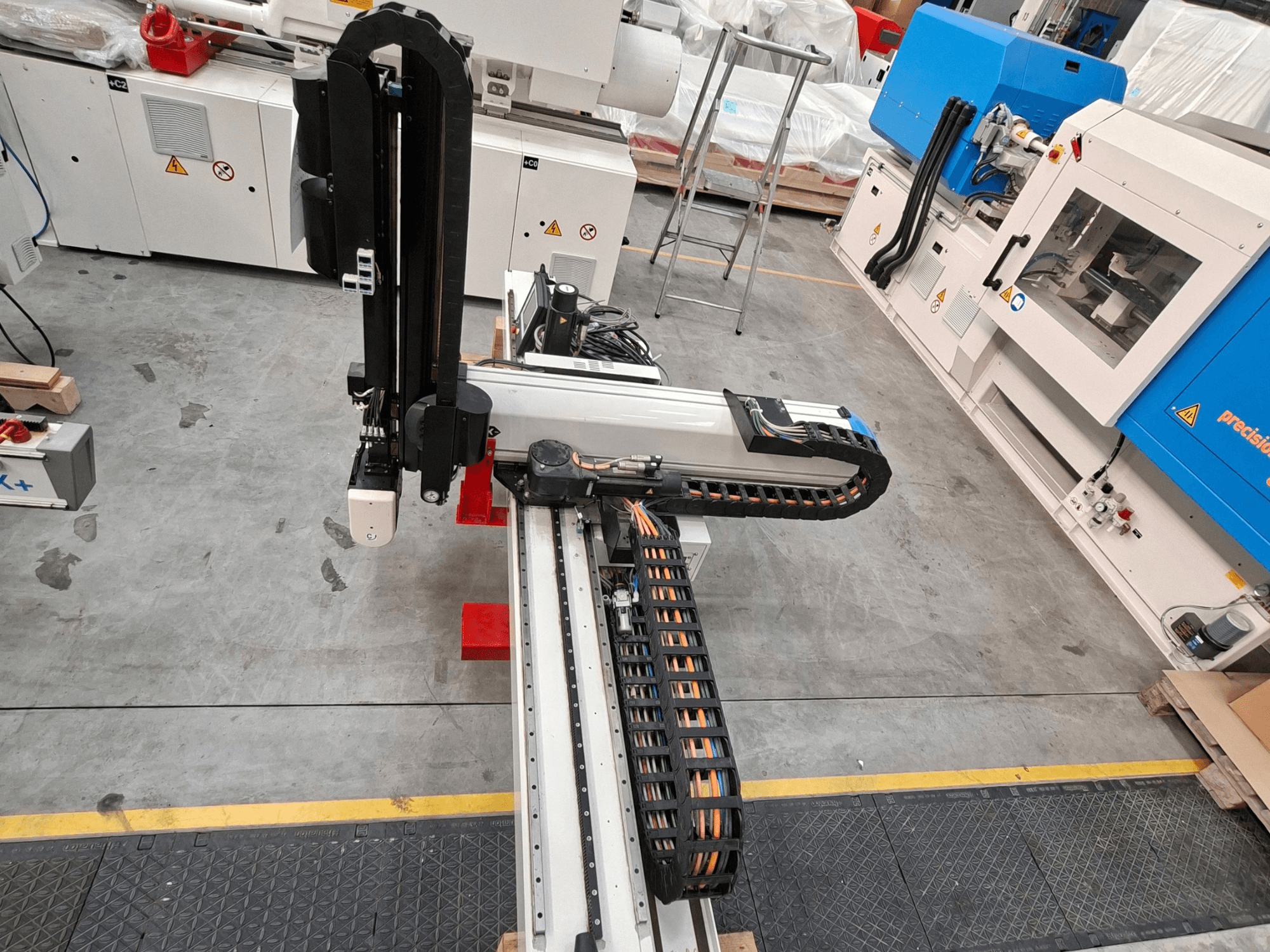 Macchina per la lavorazione della plastica Krauss Maffei LRX150-MC5 vista dall'alto, con in primo piano il braccio robotico e la canalina per cavi sul pavimento dello stabilimento.
