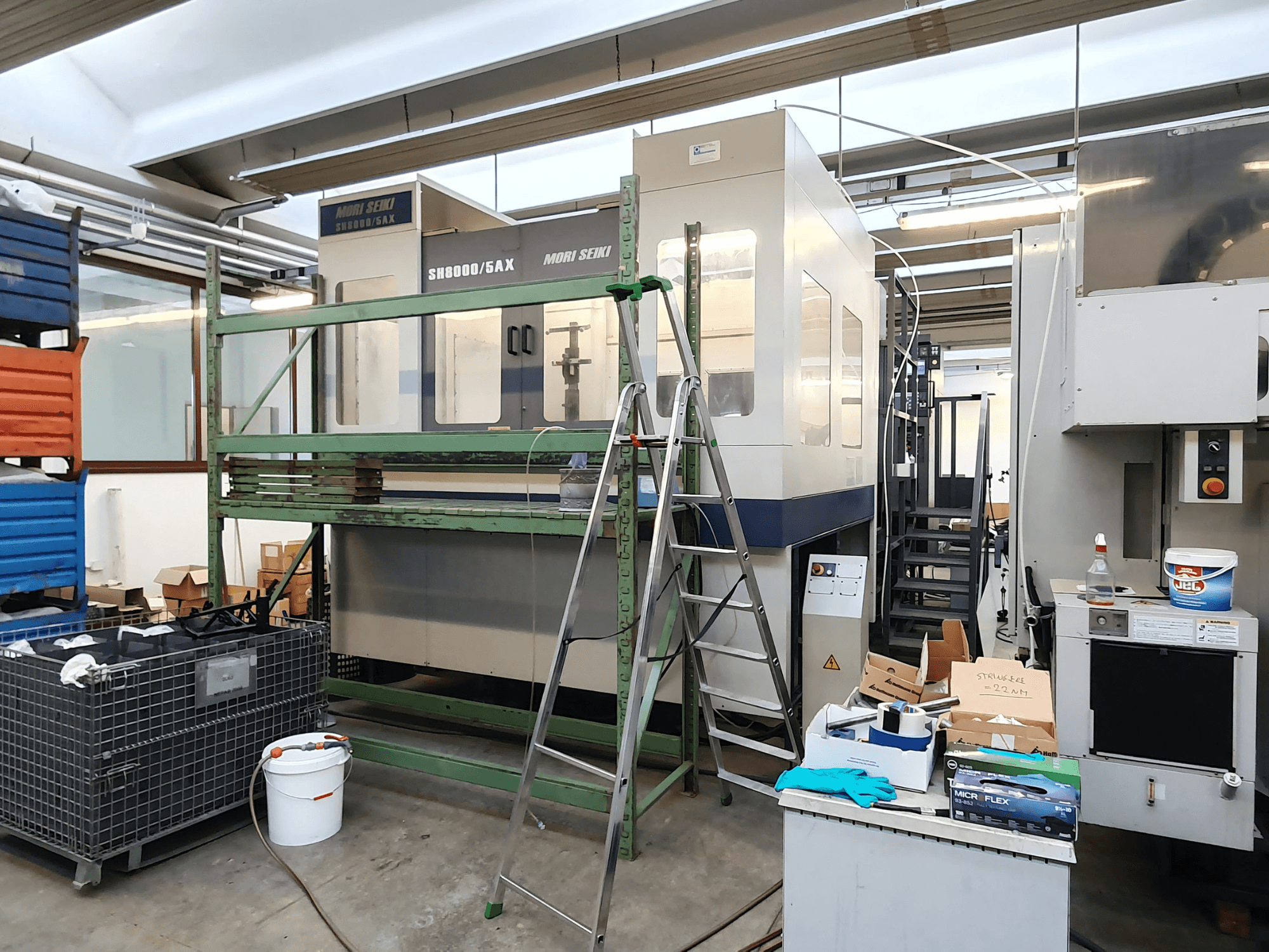 Macchina CNC Mori Seiki SH-8000/5AX in un'officina, vista frontale, con attrezzi da officina e cassette di stoccaggio nelle vicinanze.