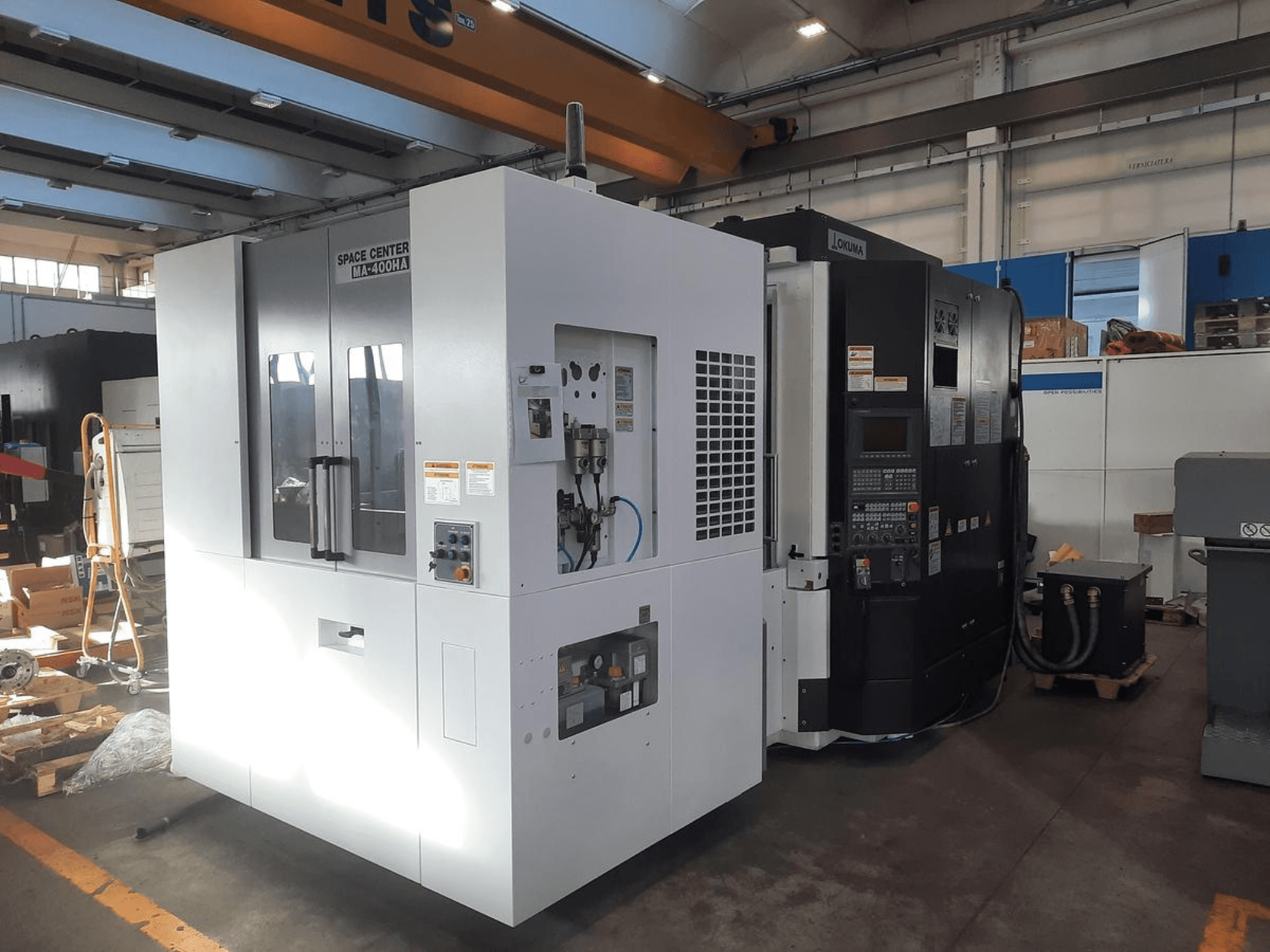 Vista frontale delle macchine CNC SPACE CENTER IM-400HAA e OKUMA, con i vari comandi e le etichette del produttore.