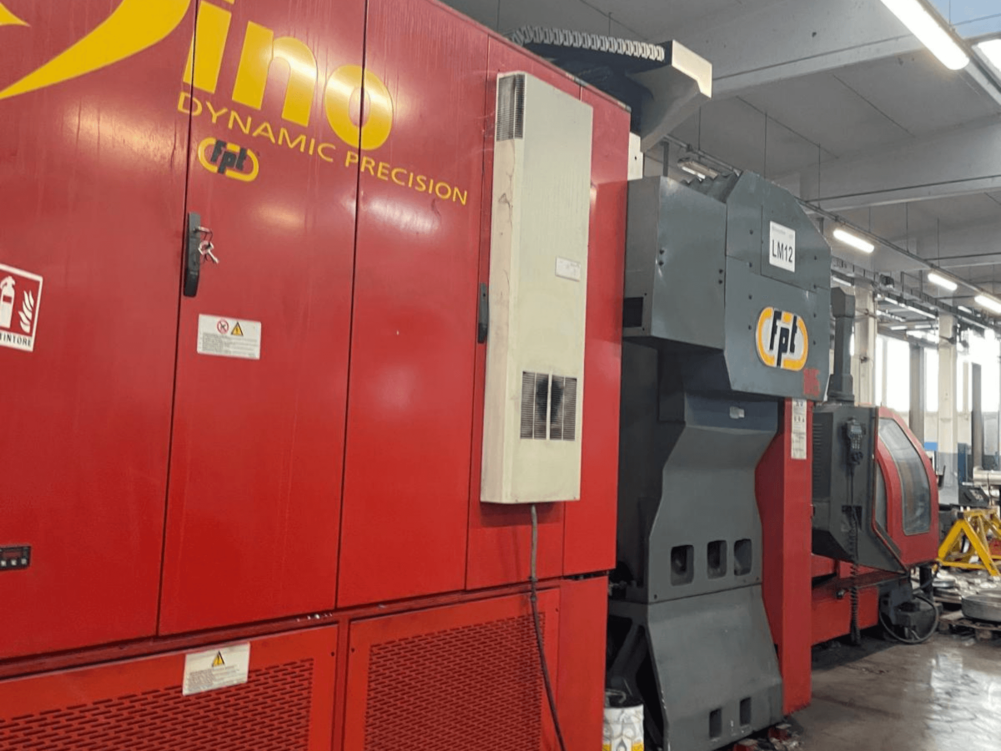 Centro di lavorazione verticale FPT DINO di colore rosso, vista laterale che mostra il pannello di controllo e l'area di lavorazione in un ambiente industriale.