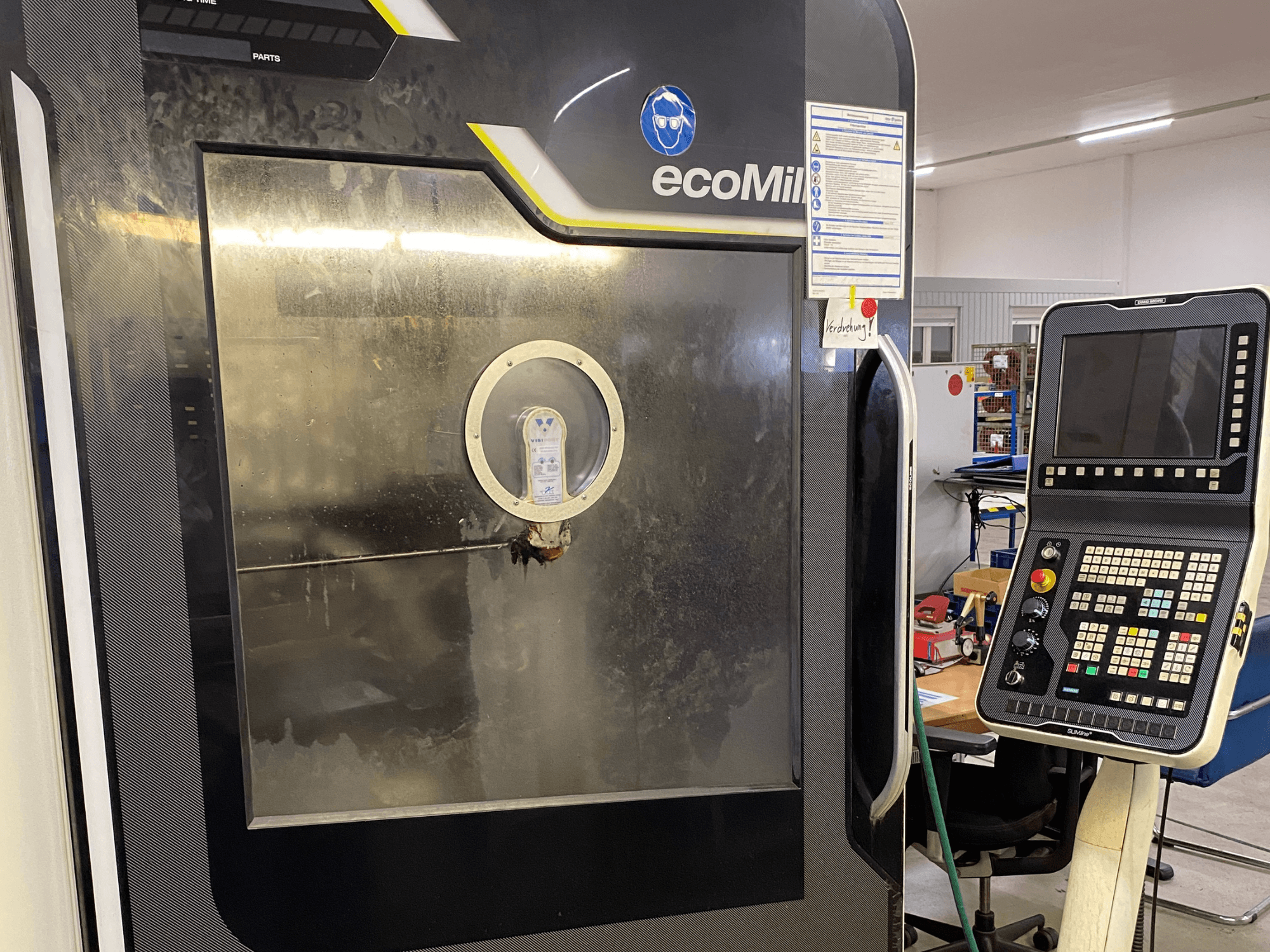 Fresatrice DMG MU 70 ECO vista frontale, con un pannello di controllo sulla destra e un pannello in vetro che lascia intravedere i componenti interni.