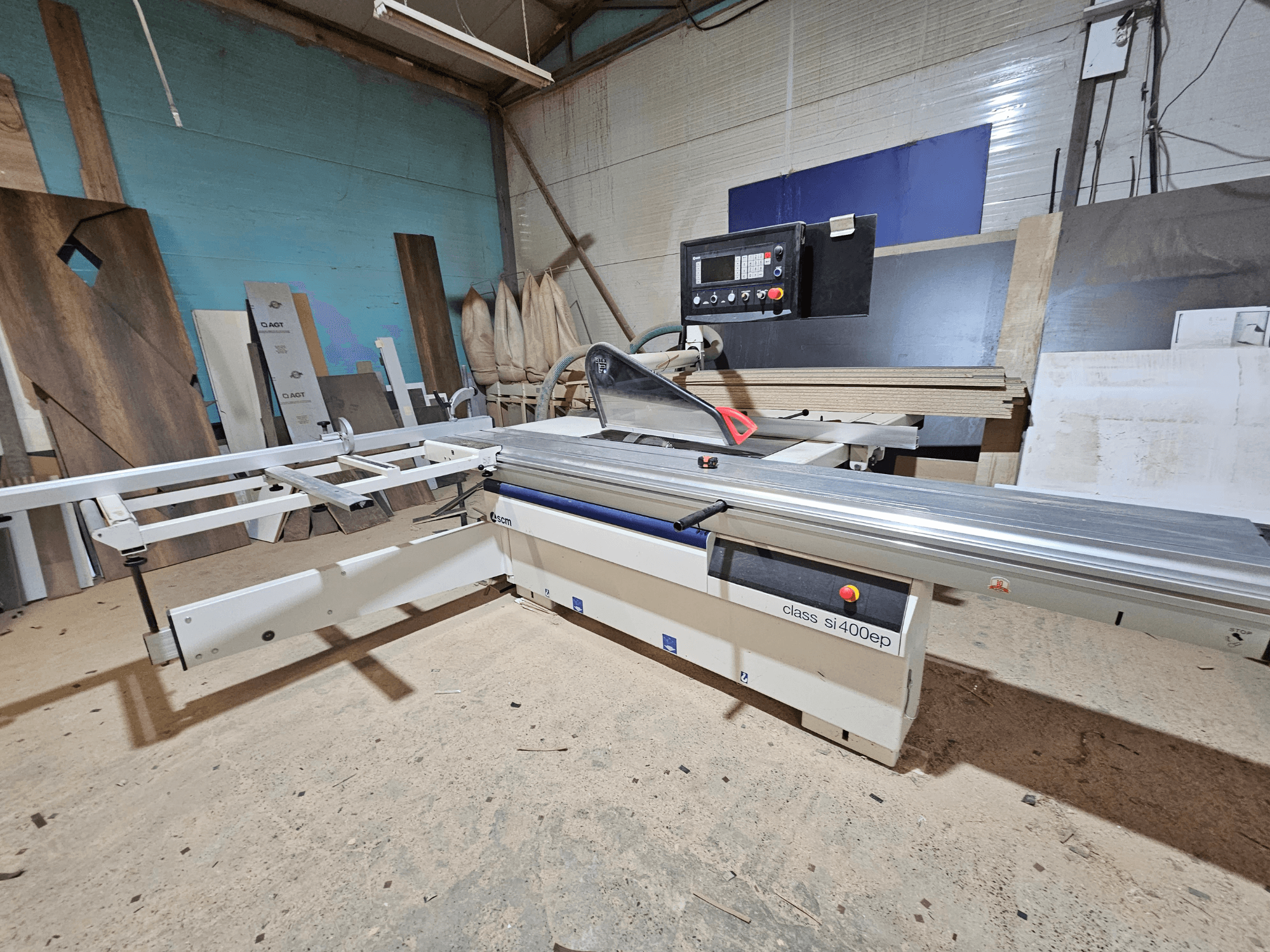 Sezionatrice di classe SI400EP, vista frontale, con recinzione regolabile, posizionata sul pavimento sabbioso dell'officina, circondata da pannelli di legno.