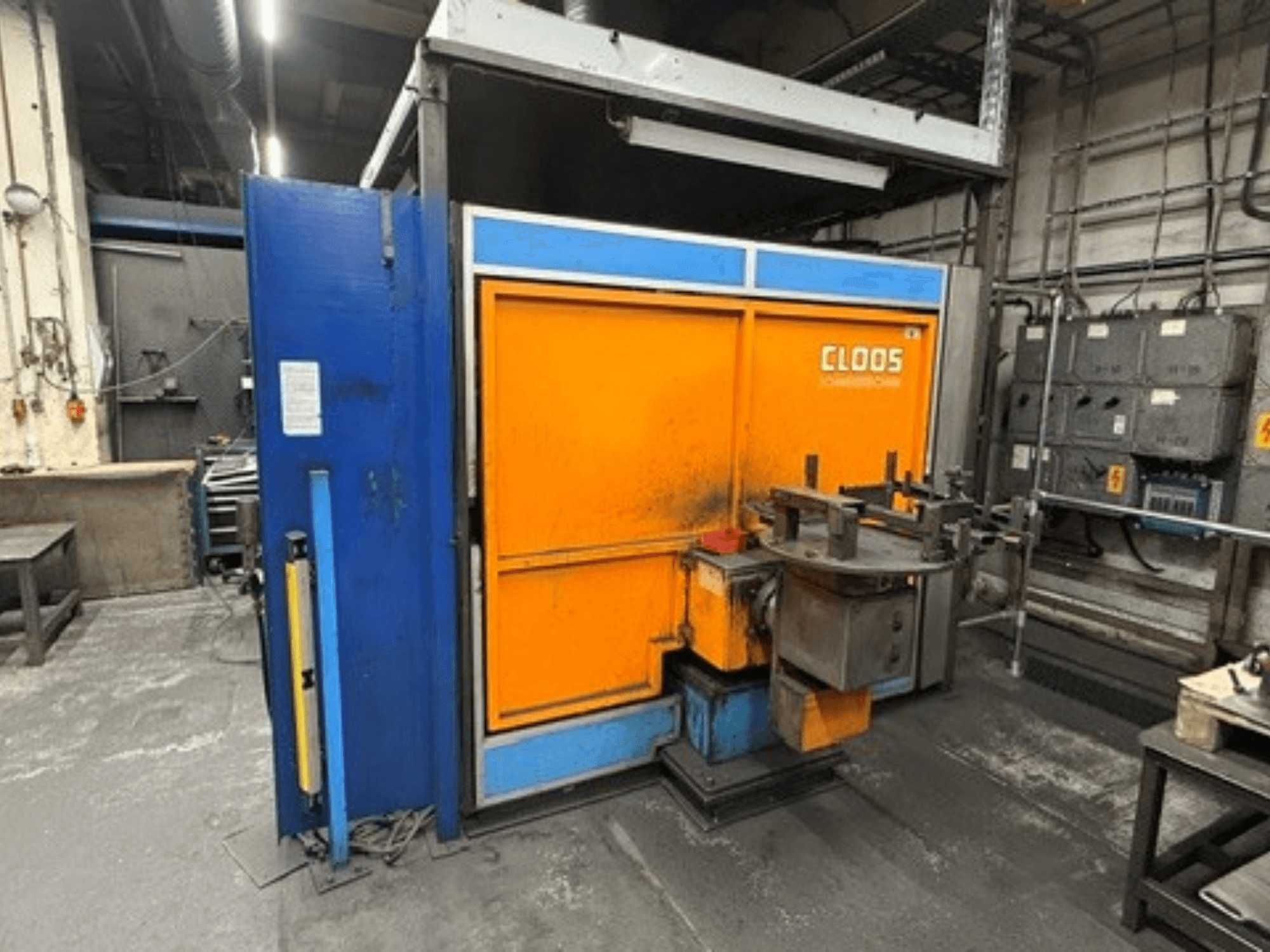 Robot di saldatura CLOOS Romat 320 in un'officina, vista frontale che mostra la struttura arancione e blu con pannello di controllo e utensili.