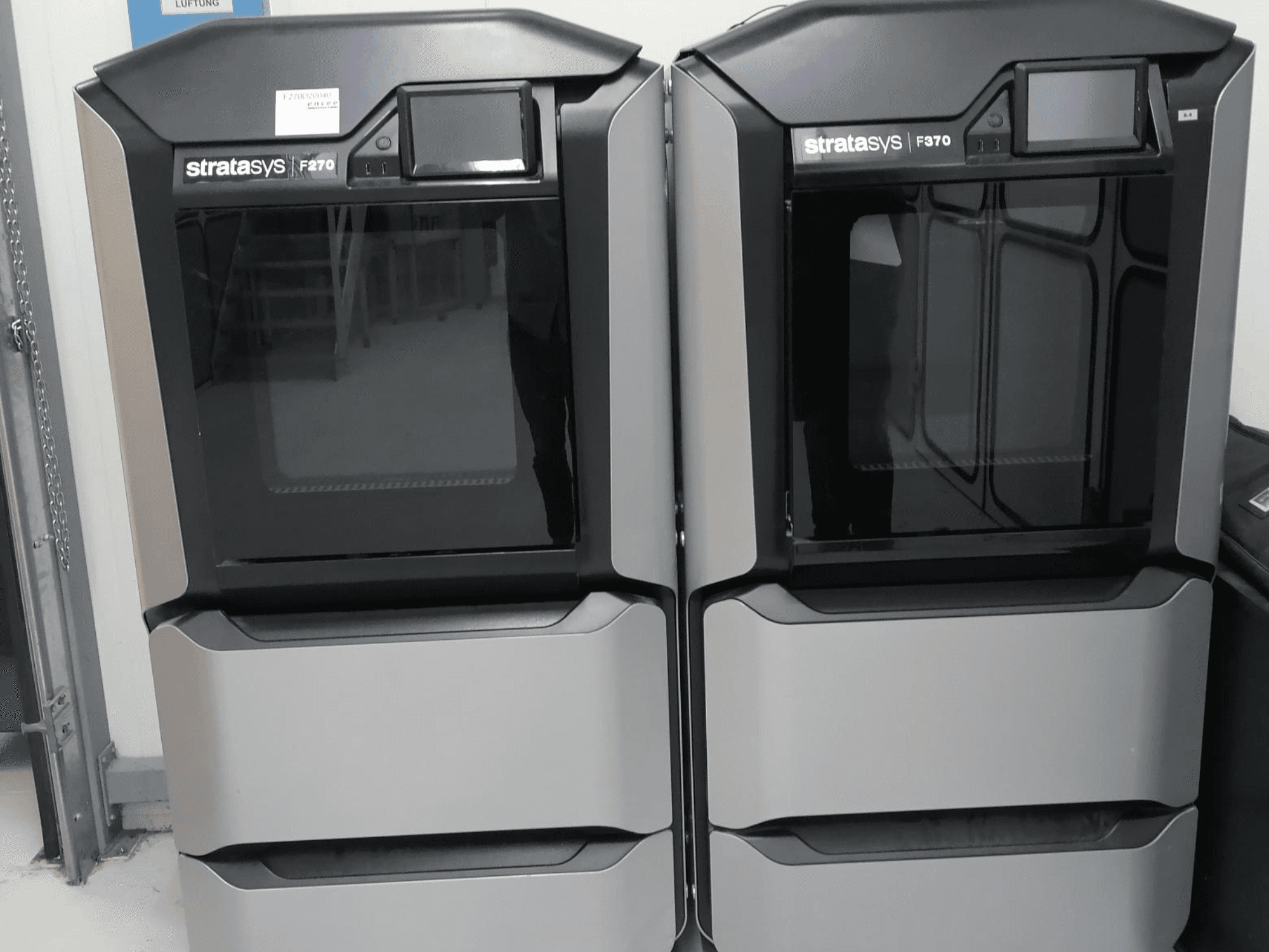 Le stampanti 3D Stratasys F370 dual plastic visualizzate in una vista frontale, caratterizzate da un elegante design nero e argento con schermi di controllo.