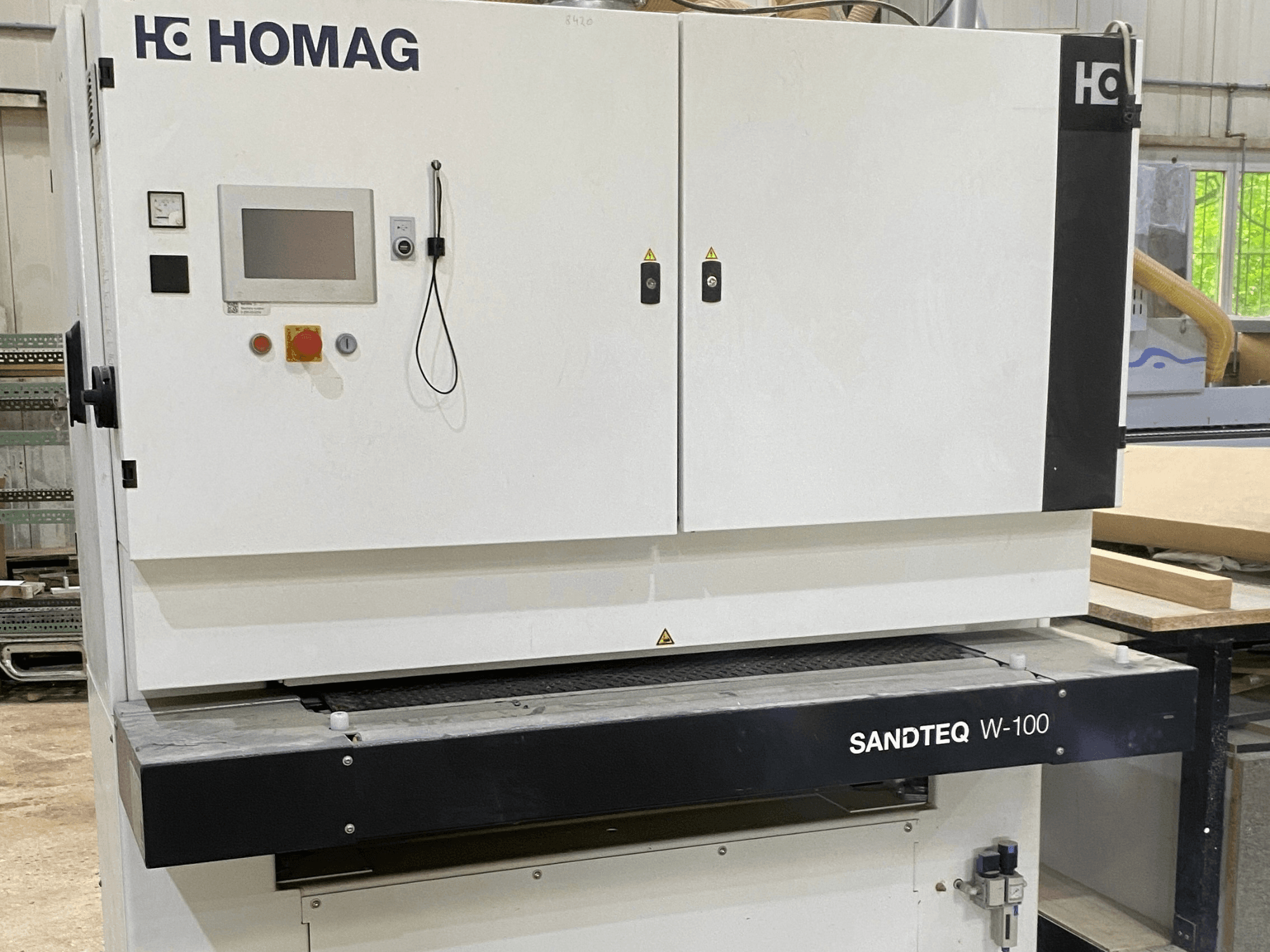 Levigatrice a nastro HOMAG SANDTEQ W-100 in un'officina, con in primo piano il pannello di controllo, l'uscita per la polvere e l'area del nastro abrasivo. Vista frontale.