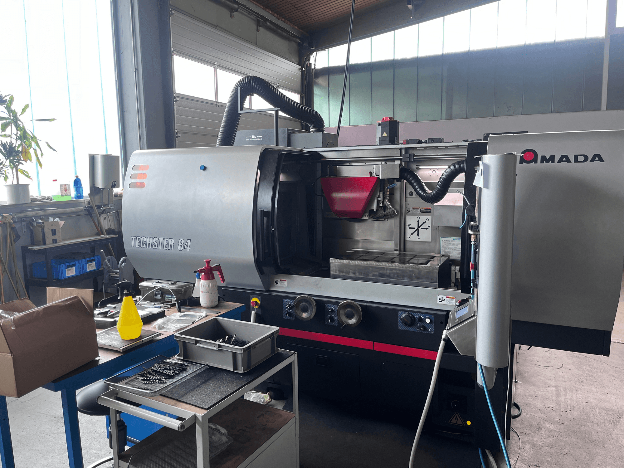 Rettificatrice piana AMADA Techster 84 in un'officina, con vista frontale che mostra i comandi operativi e la tramoggia rossa.