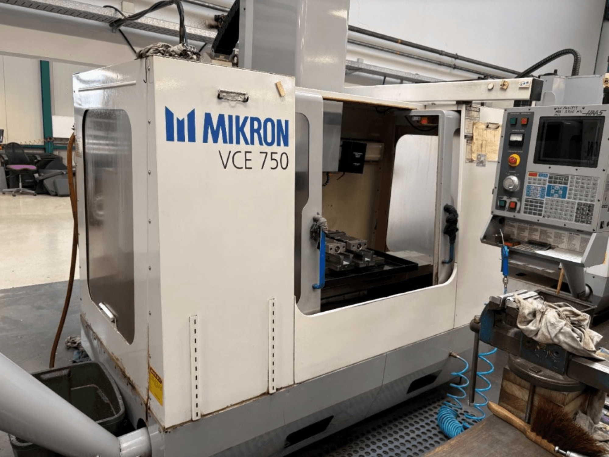 Vista frontale della fresatrice CNC Mikron VCE 750, con piano di lavoro lavorato e pannello di controllo con vari pulsanti e schermate.