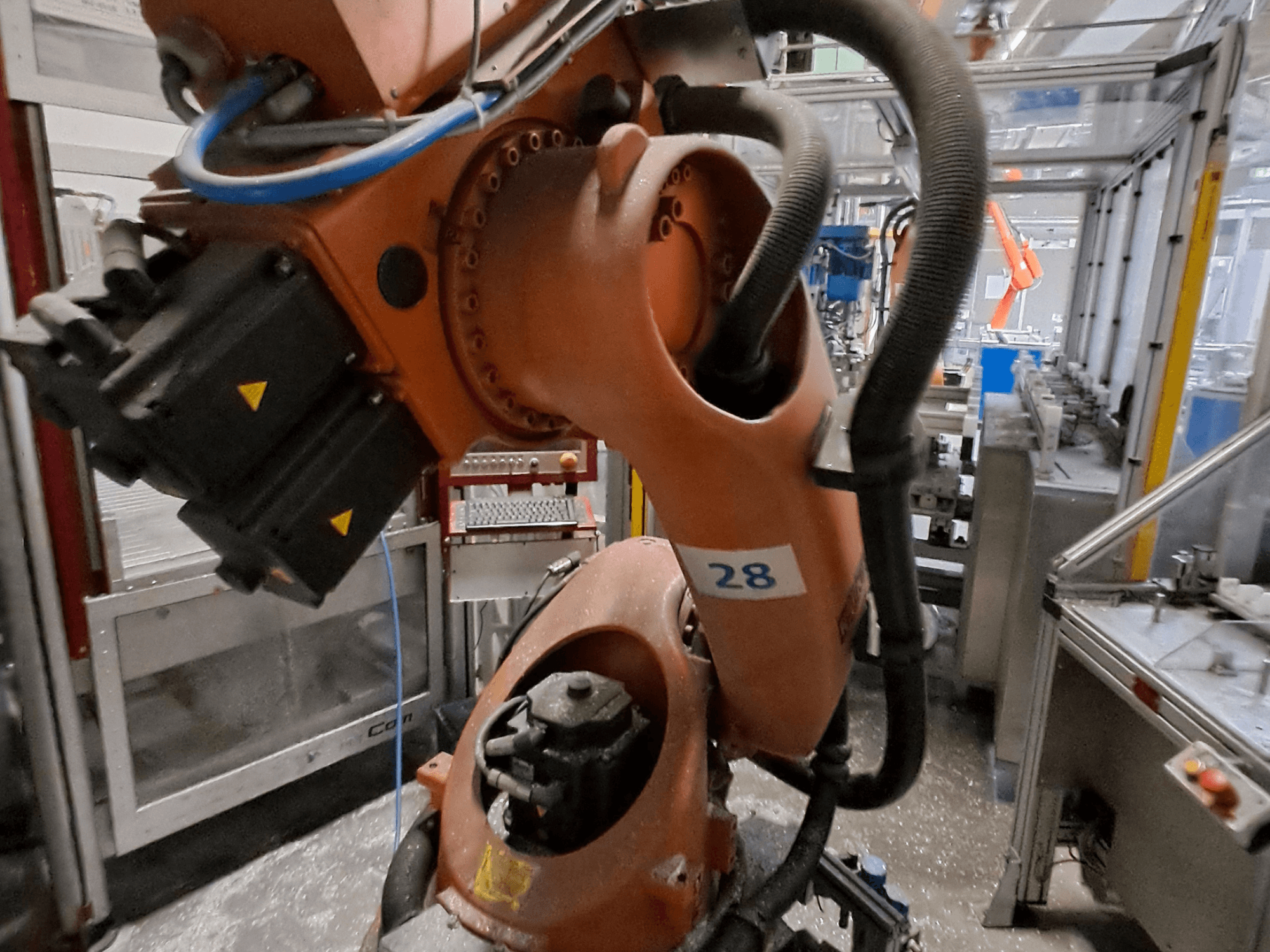 Primo piano del braccio robotico KUKA KR30-3, con corpo arancione, contrassegnato dal numero 28, che mostra i motori e il cablaggio in una vista laterale.
