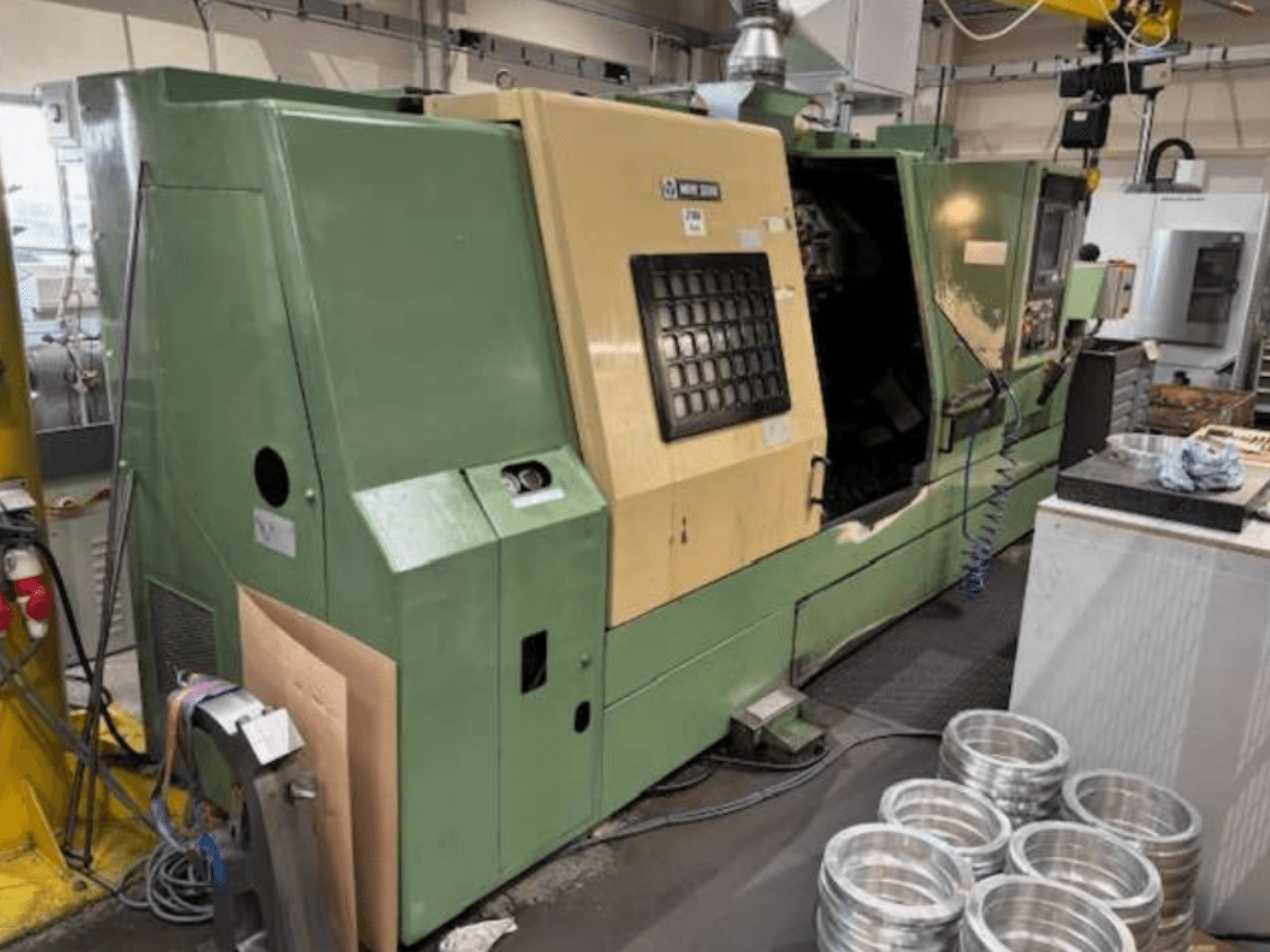 Tornio CNC verde di Mazak, visto dal davanti, che mostra un pannello di controllo e pezzi di alluminio lavorati su un piano di lavoro.